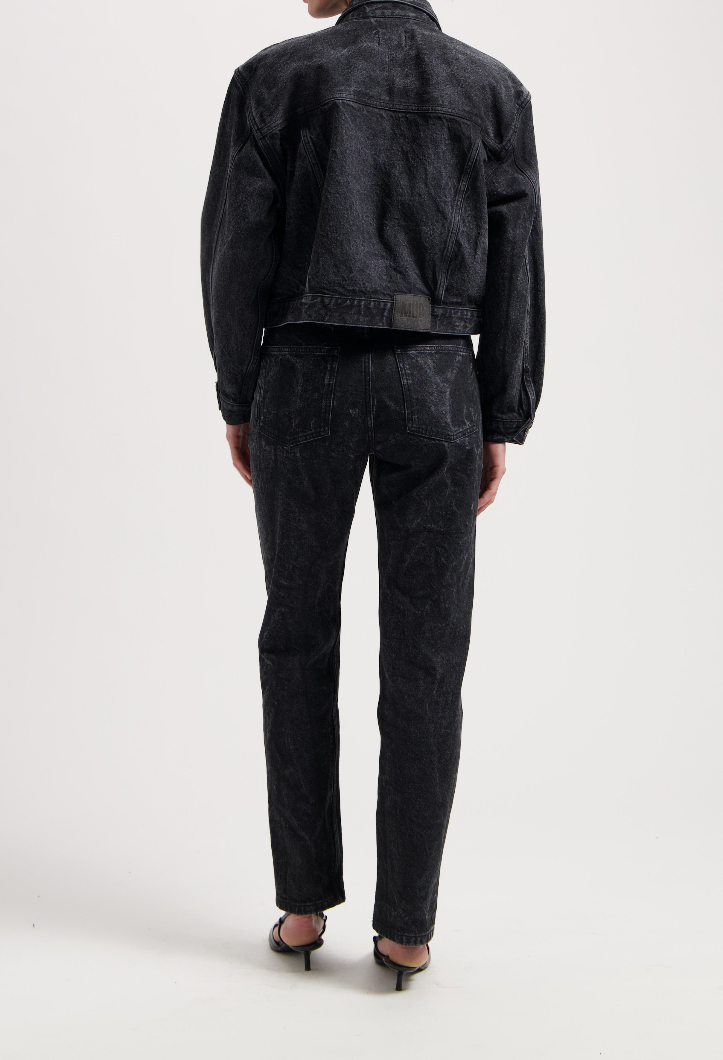 Black denim jacket and jeans set from MUD Jeans, featuring a textured finish, worn with strappy black sandals.