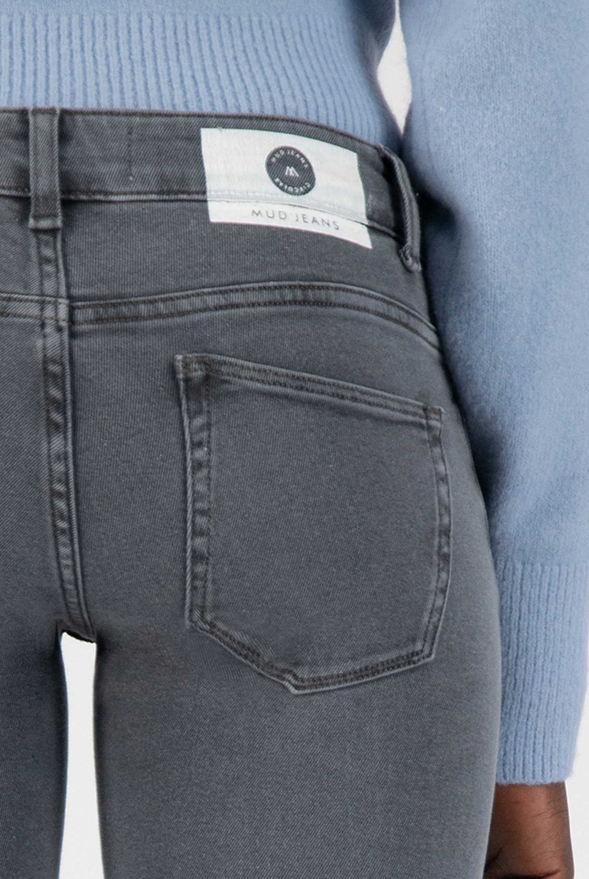 Dark gray slim-fit MUD Jeans crafted from organic cotton, featuring a back pocket detail and paired with a light blue top.