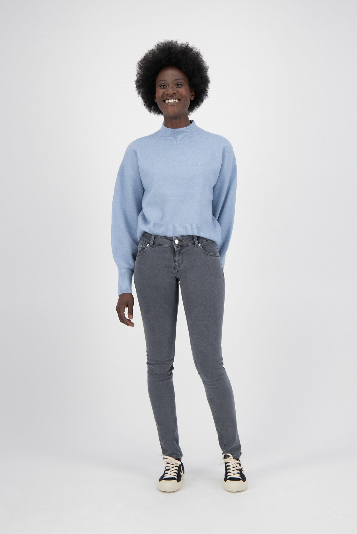 Person wearing a light blue sweater with puffed sleeves and fitted gray jeans, paired with black and white sneakers.