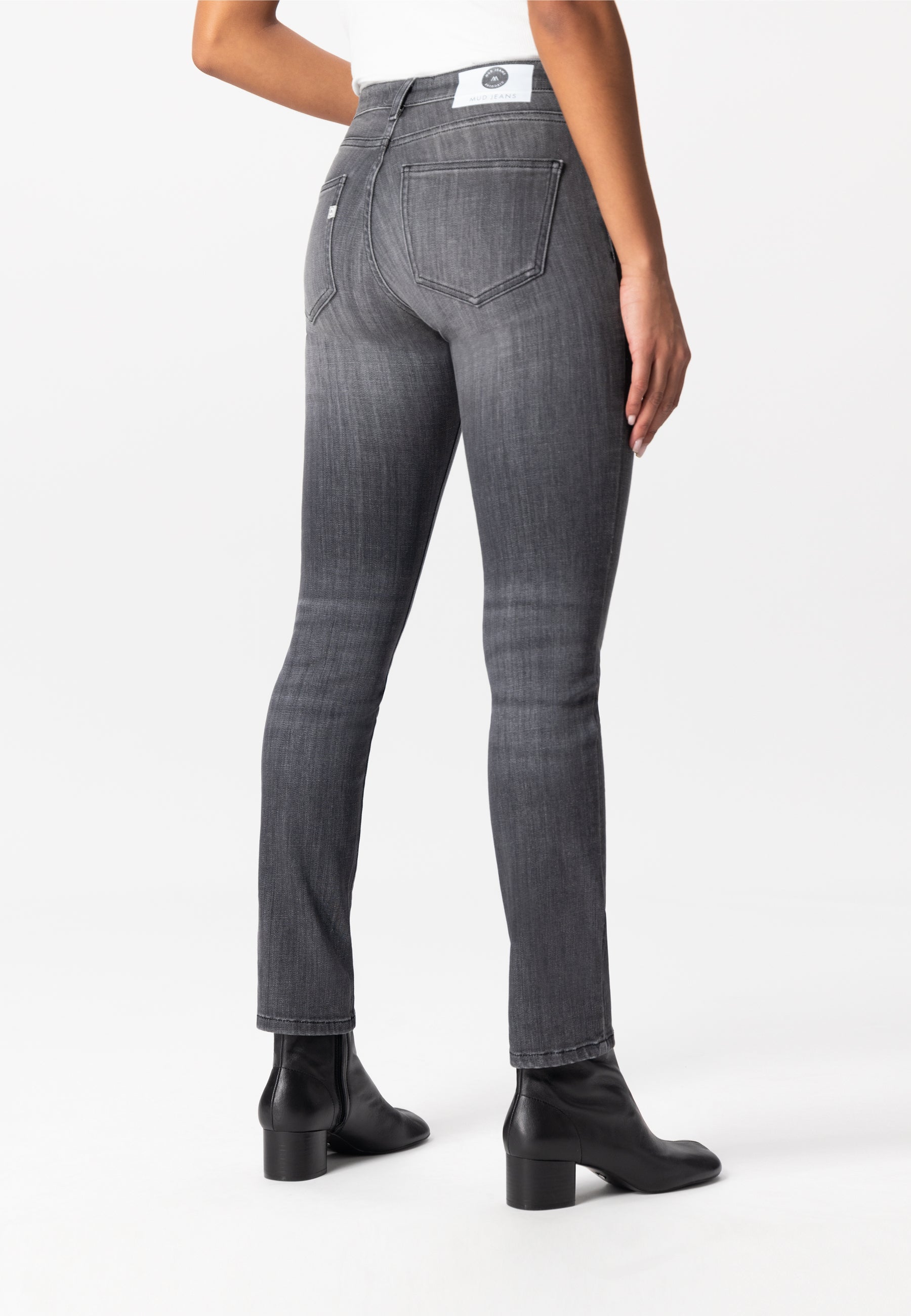 Back view of gray slim-fit MUD Jeans made from organic cotton, paired with black leather ankle boots and a white top.