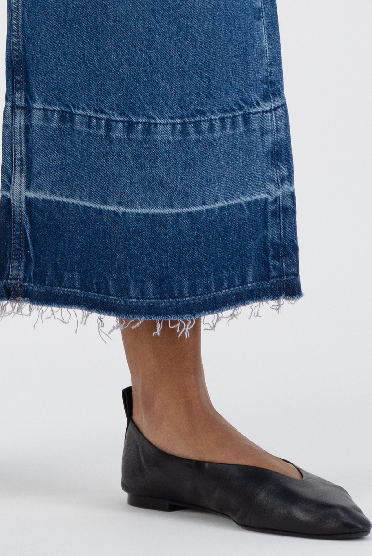 Frayed hem blue denim skirt paired with black leather flats on a neutral background, showcasing casual fashion style.
