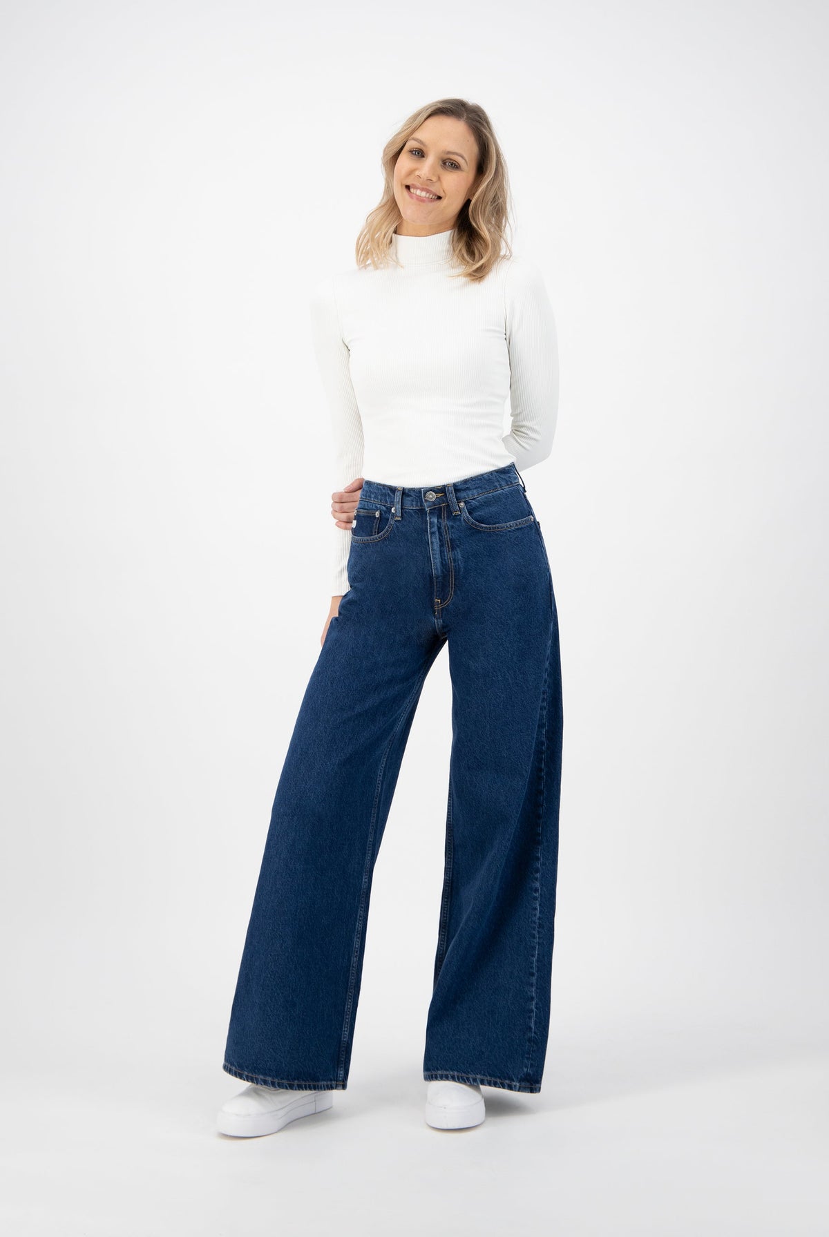 Wide-leg blue jeans worn with a fitted long-sleeve white turtleneck top, styled with casual white sneakers.