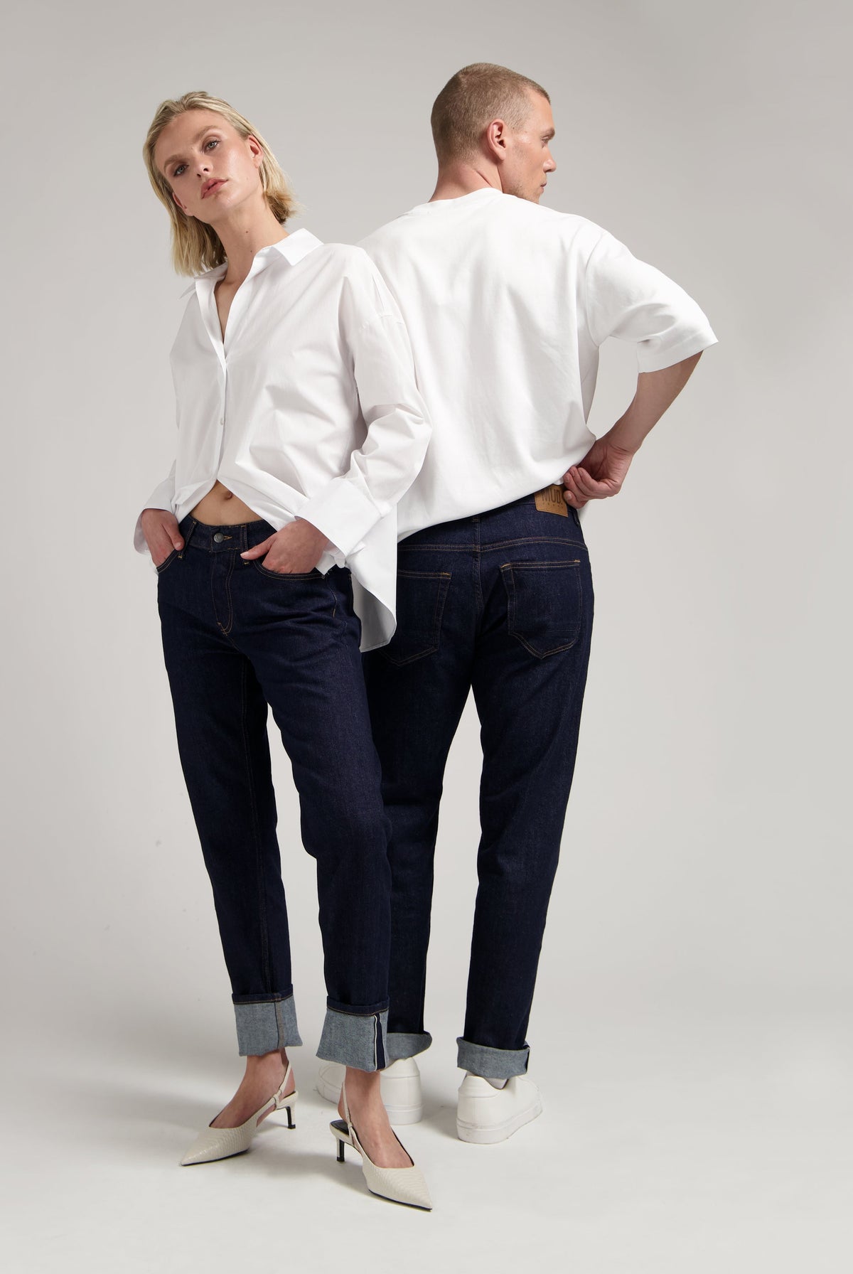 Sustainable MUD Jeans in a classic medium blue wash, crafted ethically from organic cotton, worn with a gray sweater.