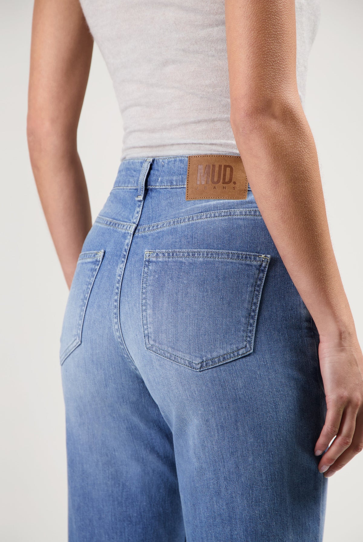 Back view of MUD Jeans made from sustainable materials, showing high-waisted, light blue denim worn with a white top.