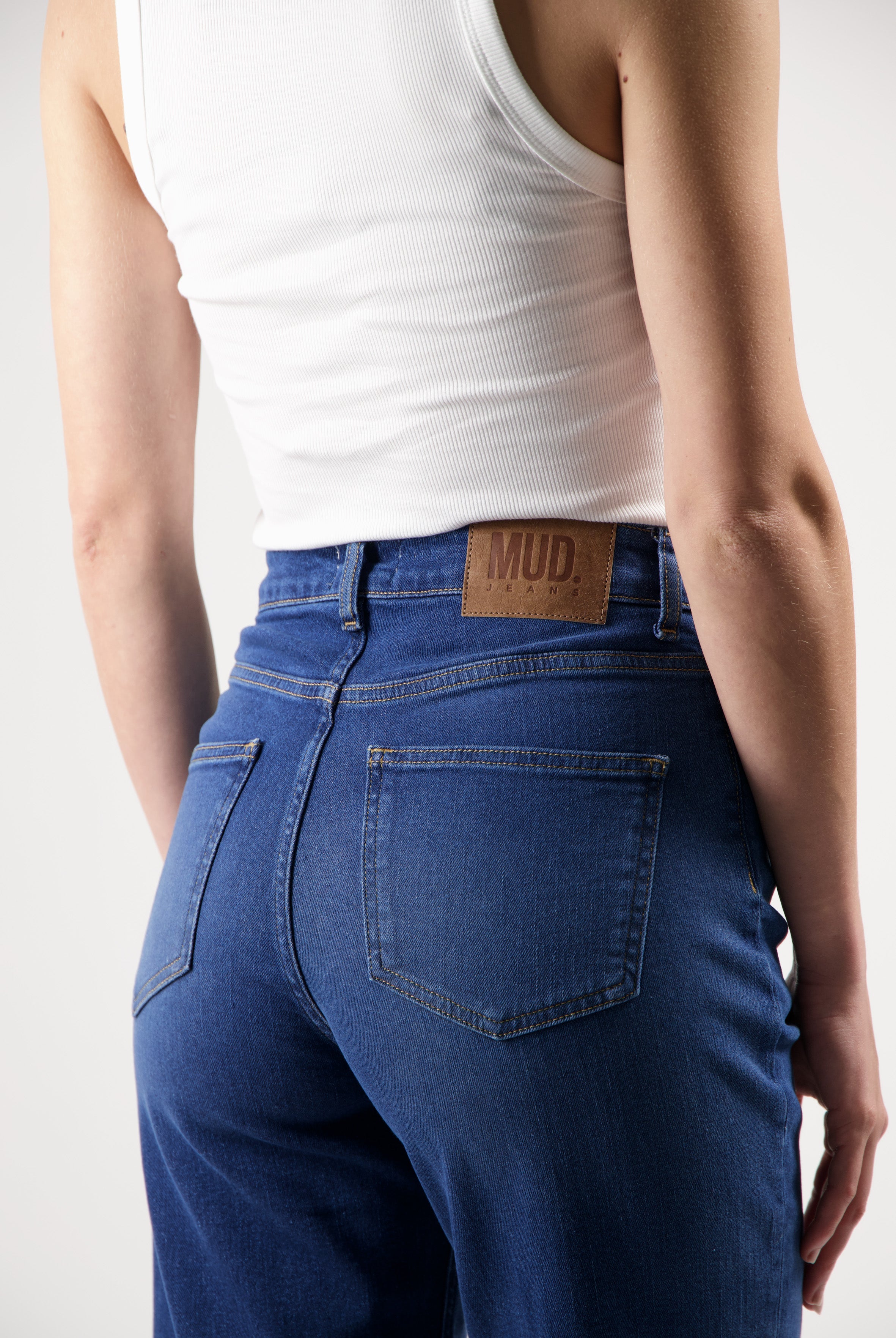 Person wearing sustainable MUD Jeans made of organic cotton with a white ribbed tank top, showcasing the denim's back details.