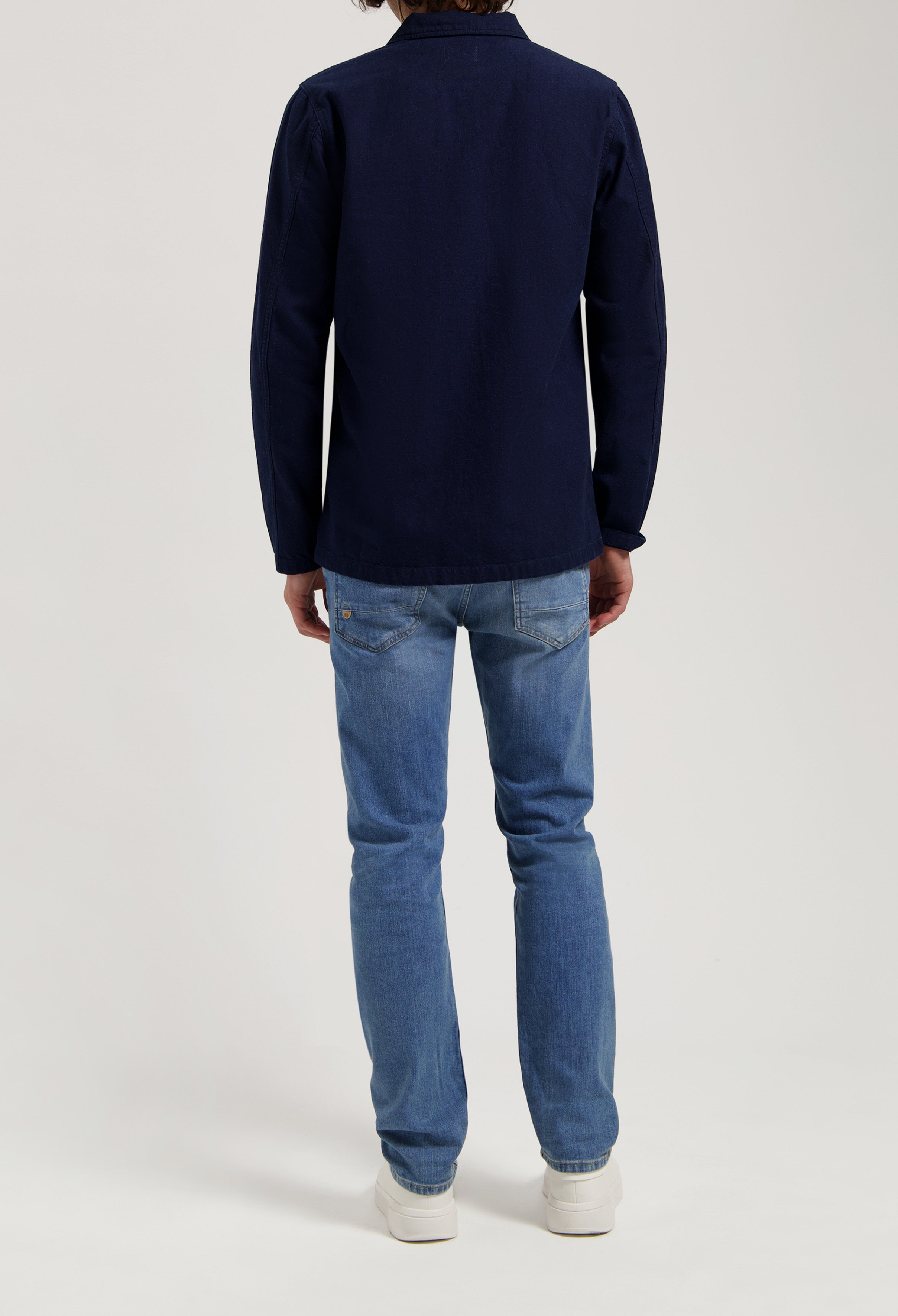 Sustainable MUD Jeans in classic fit, crafted from eco-friendly fabric, light blue denim paired with ivory knit sweater.