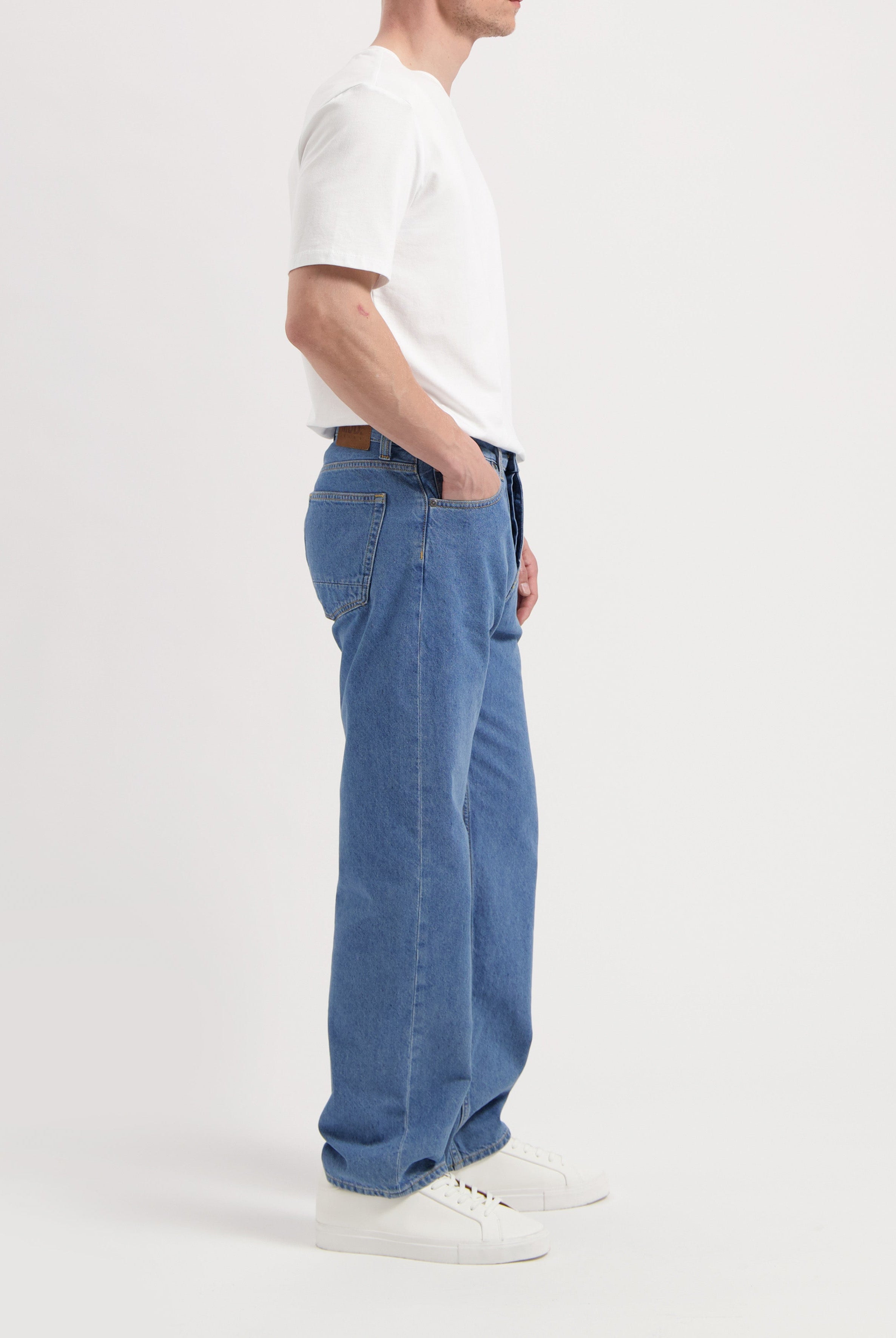 Sustainable MUD Jeans in blue denim, crafted from ethical materials, paired with a cream sweater, side profile view.