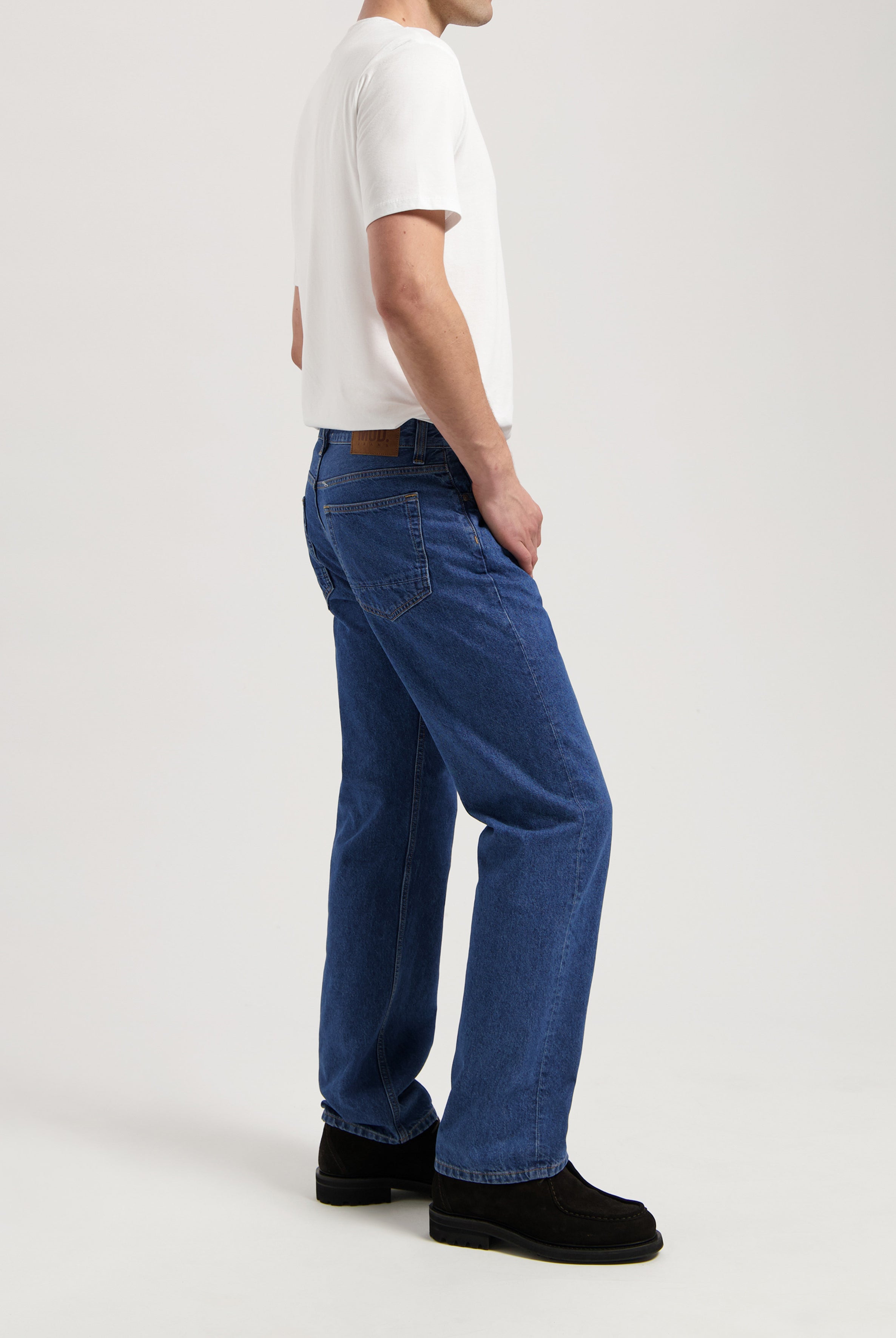 Sustainable MUD Jeans in gray denim, crafted from organic cotton, paired with a white T-shirt and black shoes.