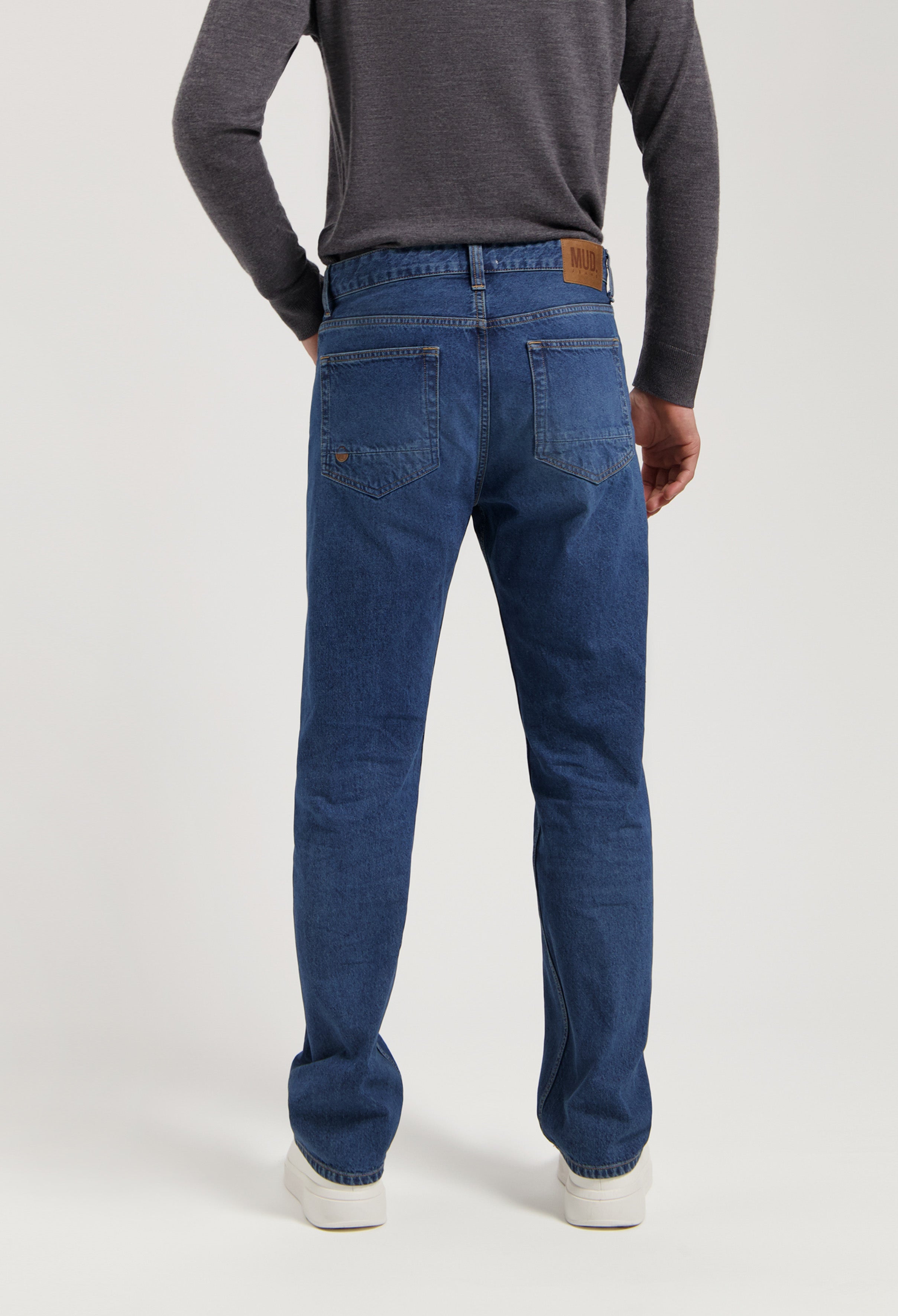 Sustainable MUD Jeans in deep blue denim, featuring a classic straight leg fit, shown with a dark gray sweater.