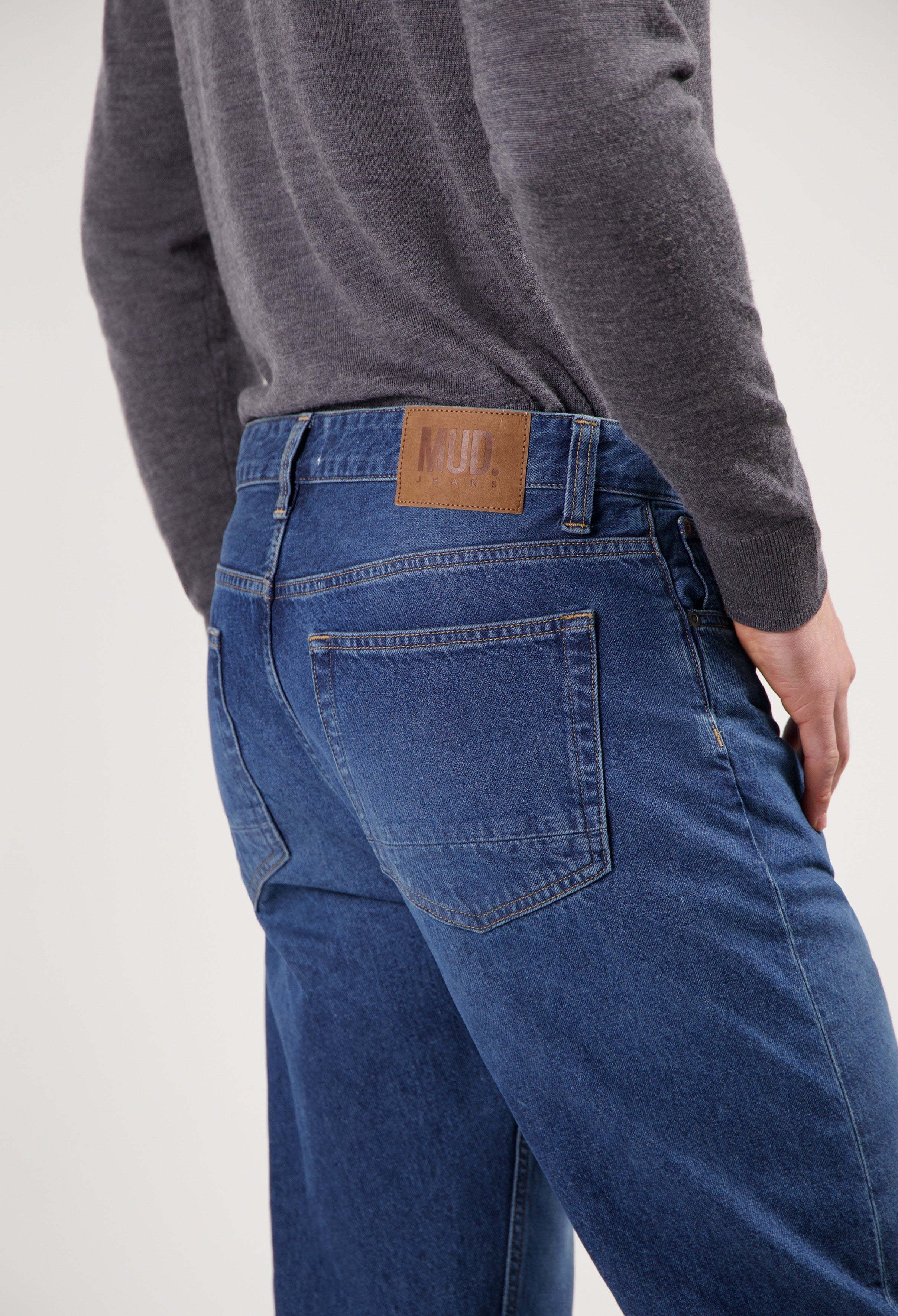 Sustainable MUD Jeans in deep blue denim, featuring ethical materials, styled with a classic cut and gray sweater.