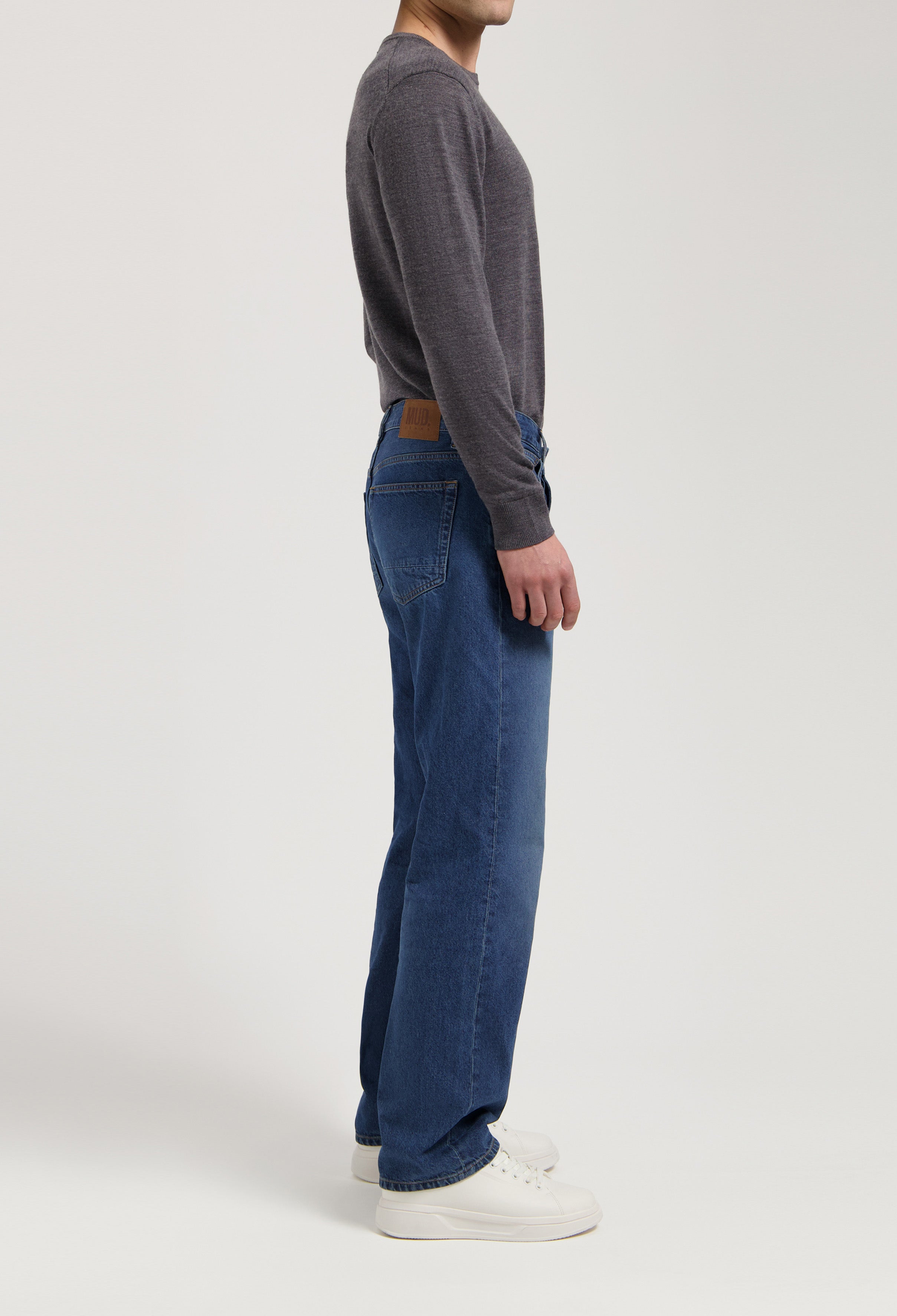 Sustainable MUD Jeans in dark blue denim, made from organic cotton, paired with a gray sweater, showcasing ethical fashion.