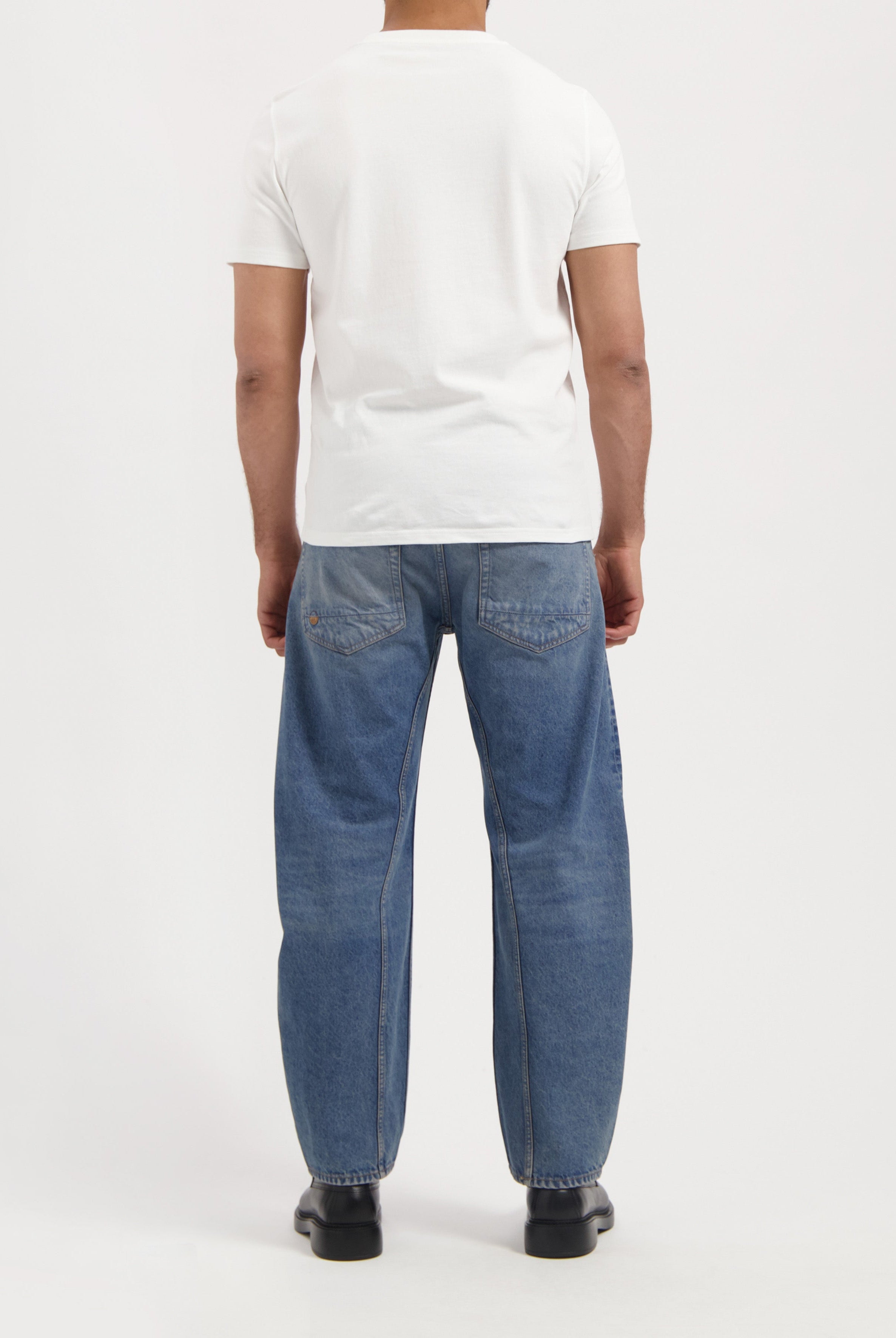 Sustainable MUD Jeans crafted from organic cotton, featuring mid-blue denim in a slim fit, worn with black shoes.
