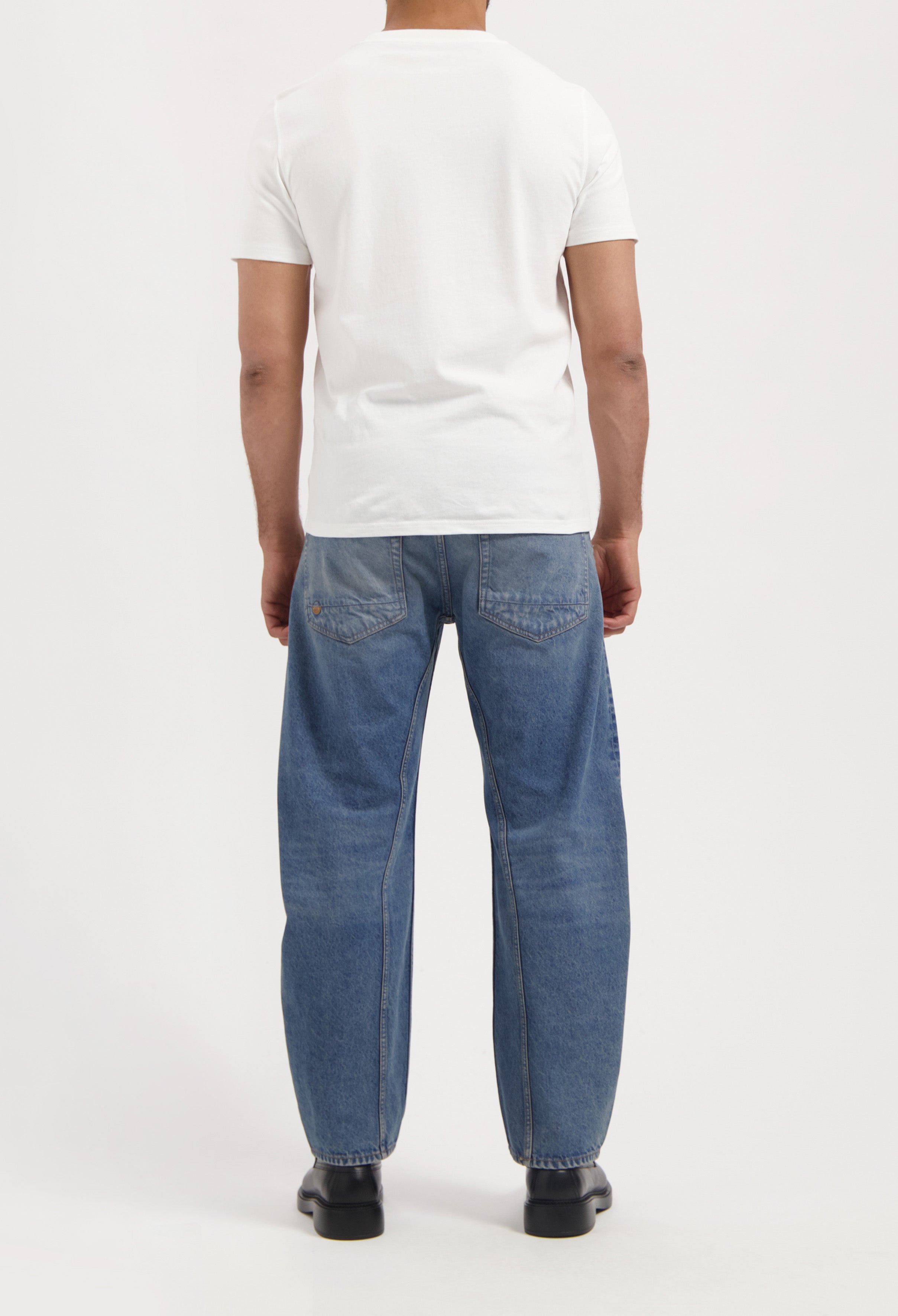 Sustainable MUD Jeans crafted from organic cotton, featuring mid-blue denim in a slim fit, worn with black shoes.