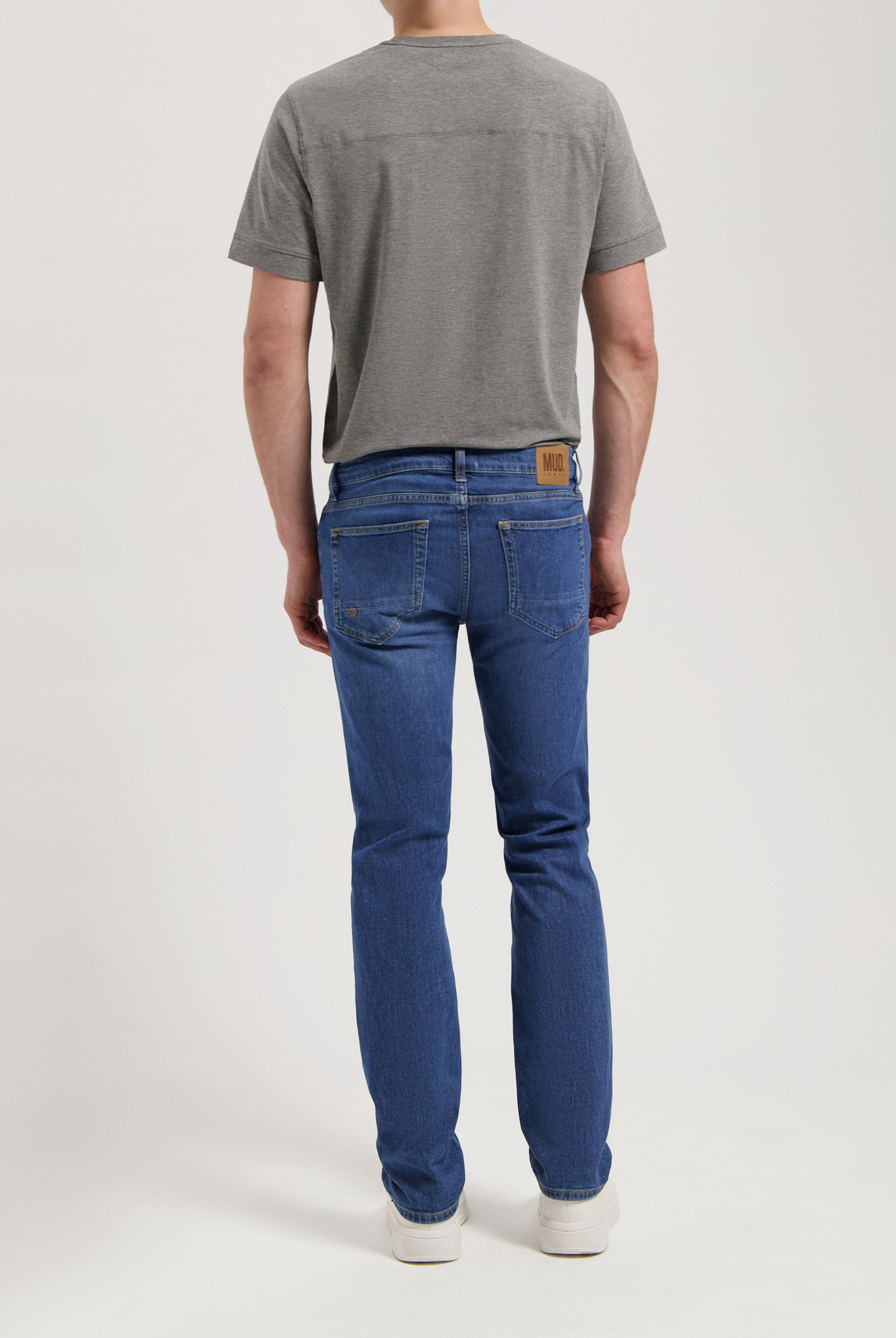 Sustainable Mud Jeans in beige, tailored fit crafted from organic cotton, paired with a simple gray t-shirt and casual sneakers.