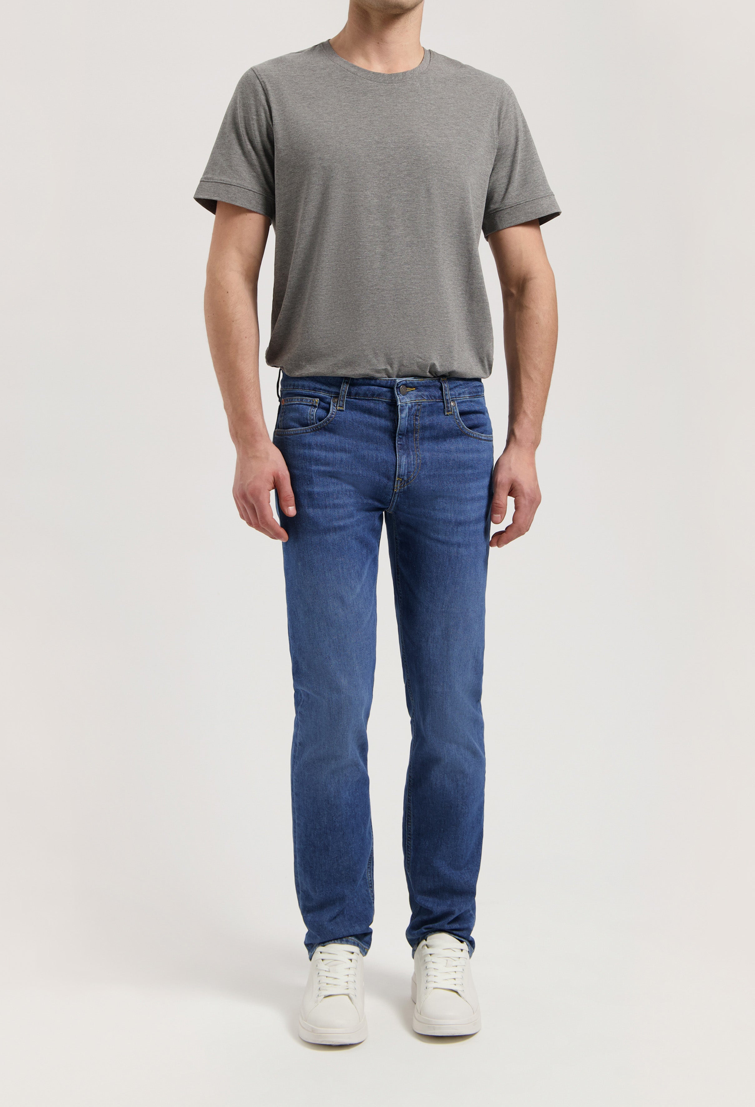Sustainable MUD Jeans, dark blue slim-fit, crafted from organic cotton, paired with a white tee and white sneakers.