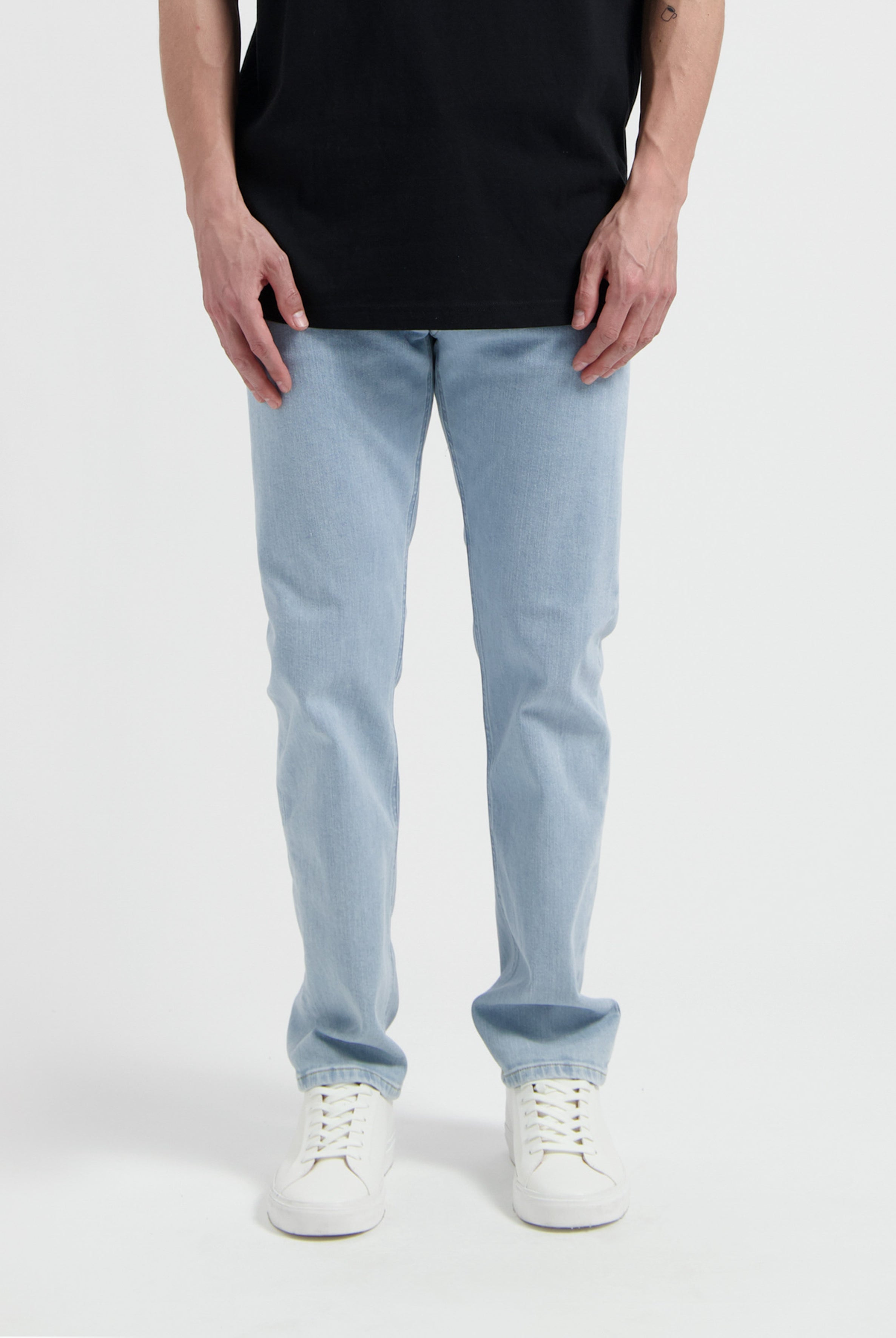 Sustainable MUD Jeans in light blue denim, crafted from organic cotton, worn with a cream sweater and black shoes.