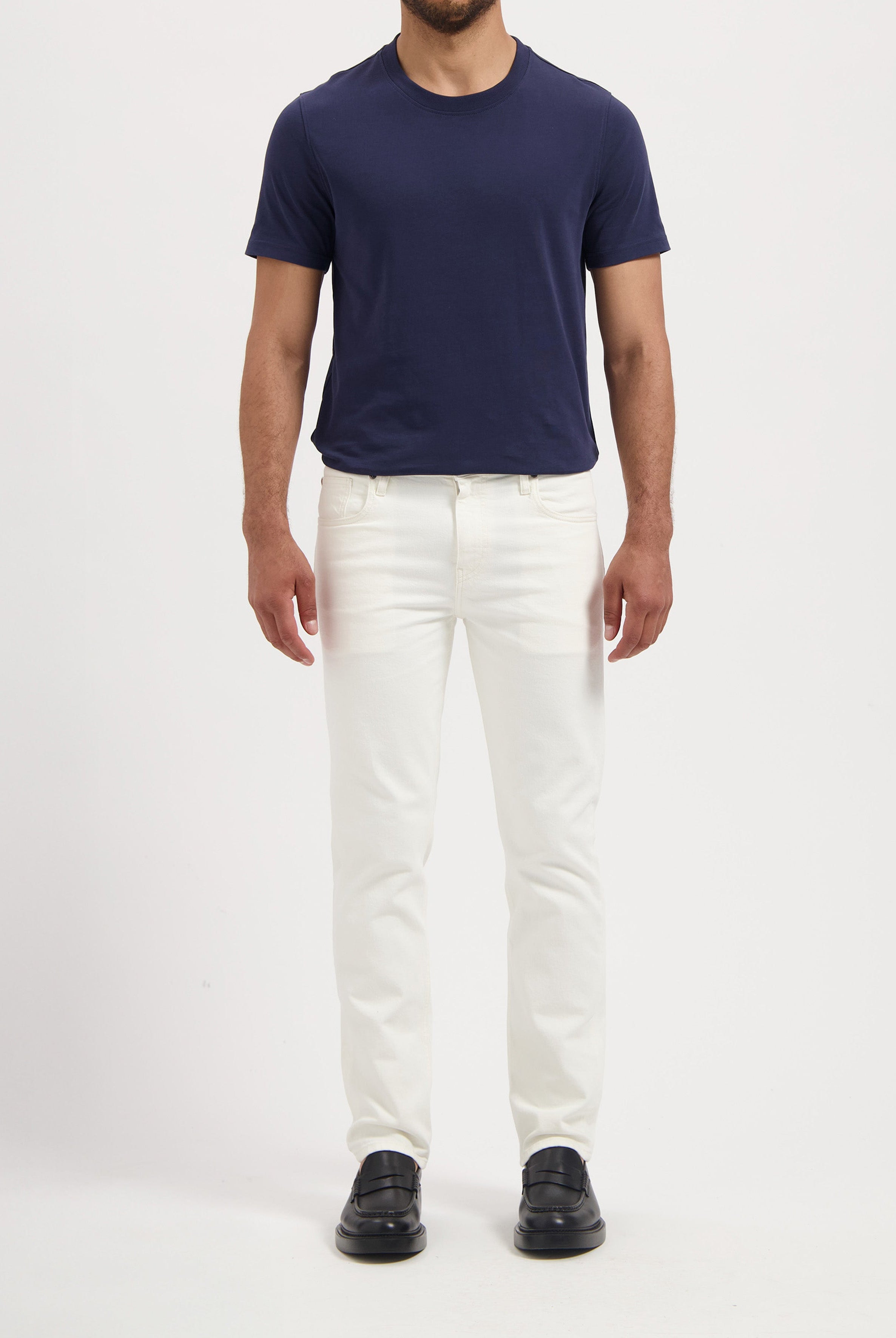 Sustainable MUD Jeans in a slim, white cotton design, paired with a navy t-shirt and black loafers for a classic look.