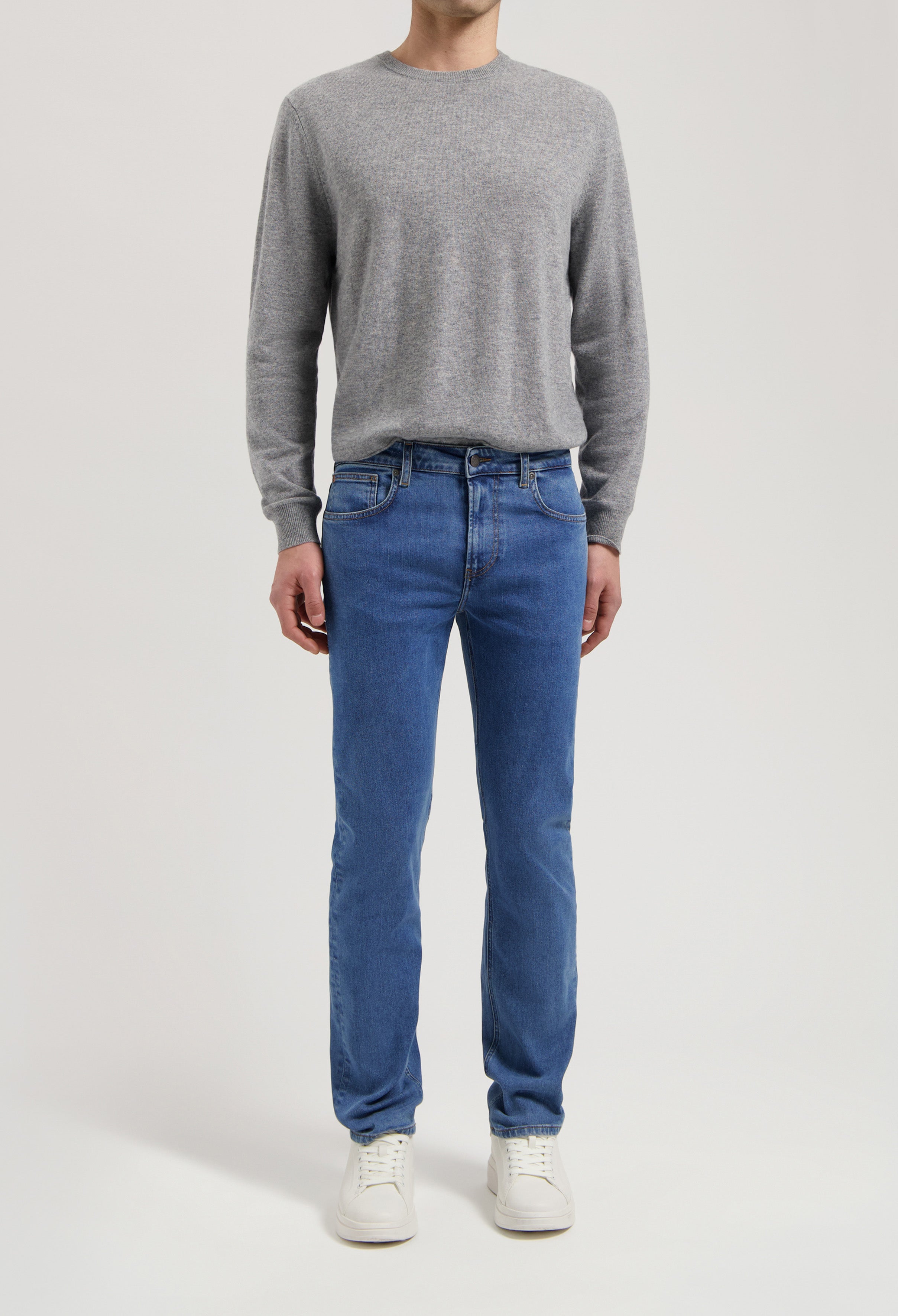 Sustainable MUD Jeans in classic blue denim, crafted from organic cotton, paired with a gray sweater for an ethical style.