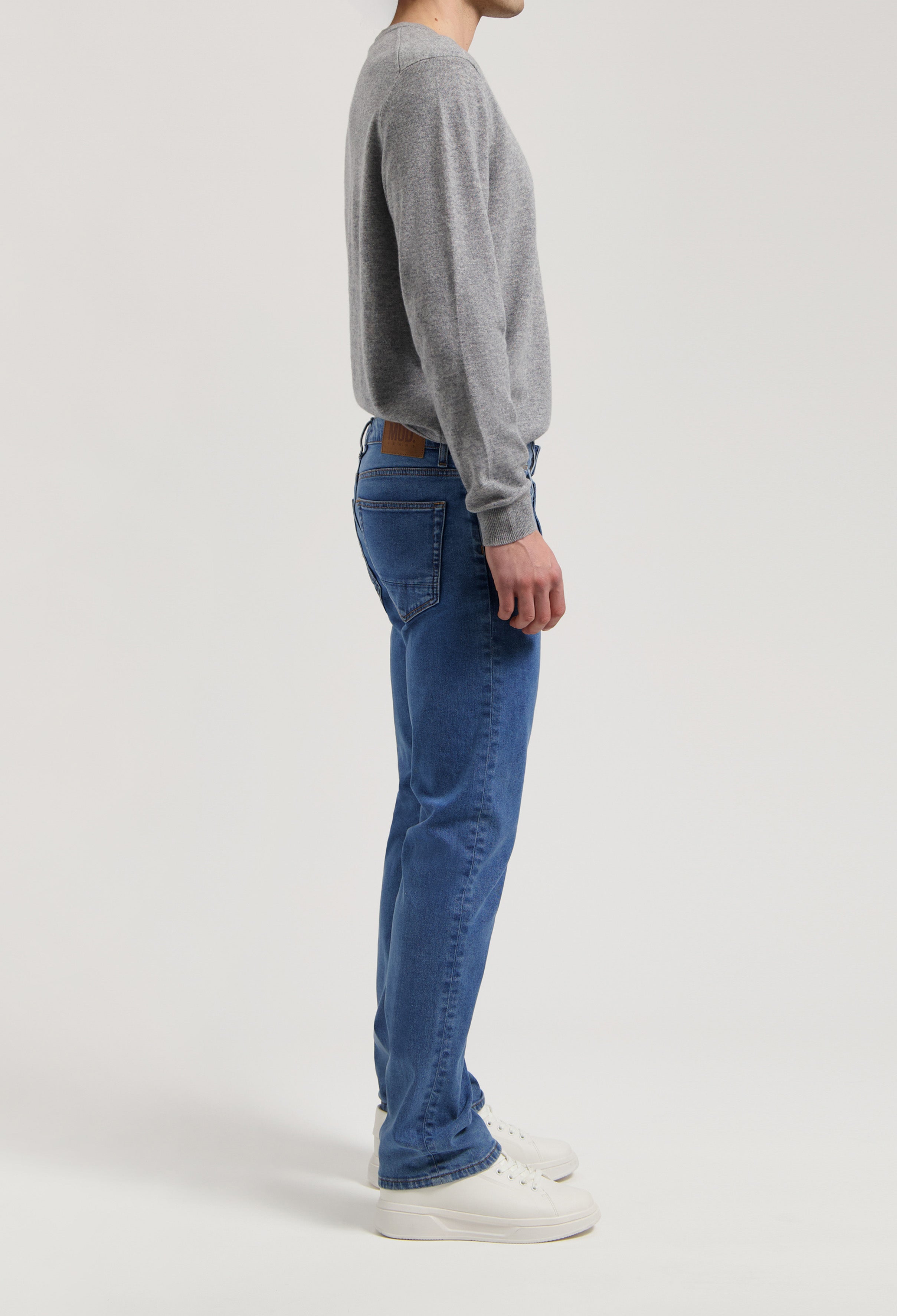 Sustainable MUD Jeans in a classic blue denim, ethically made, paired with a light gray sweater and white sneakers.