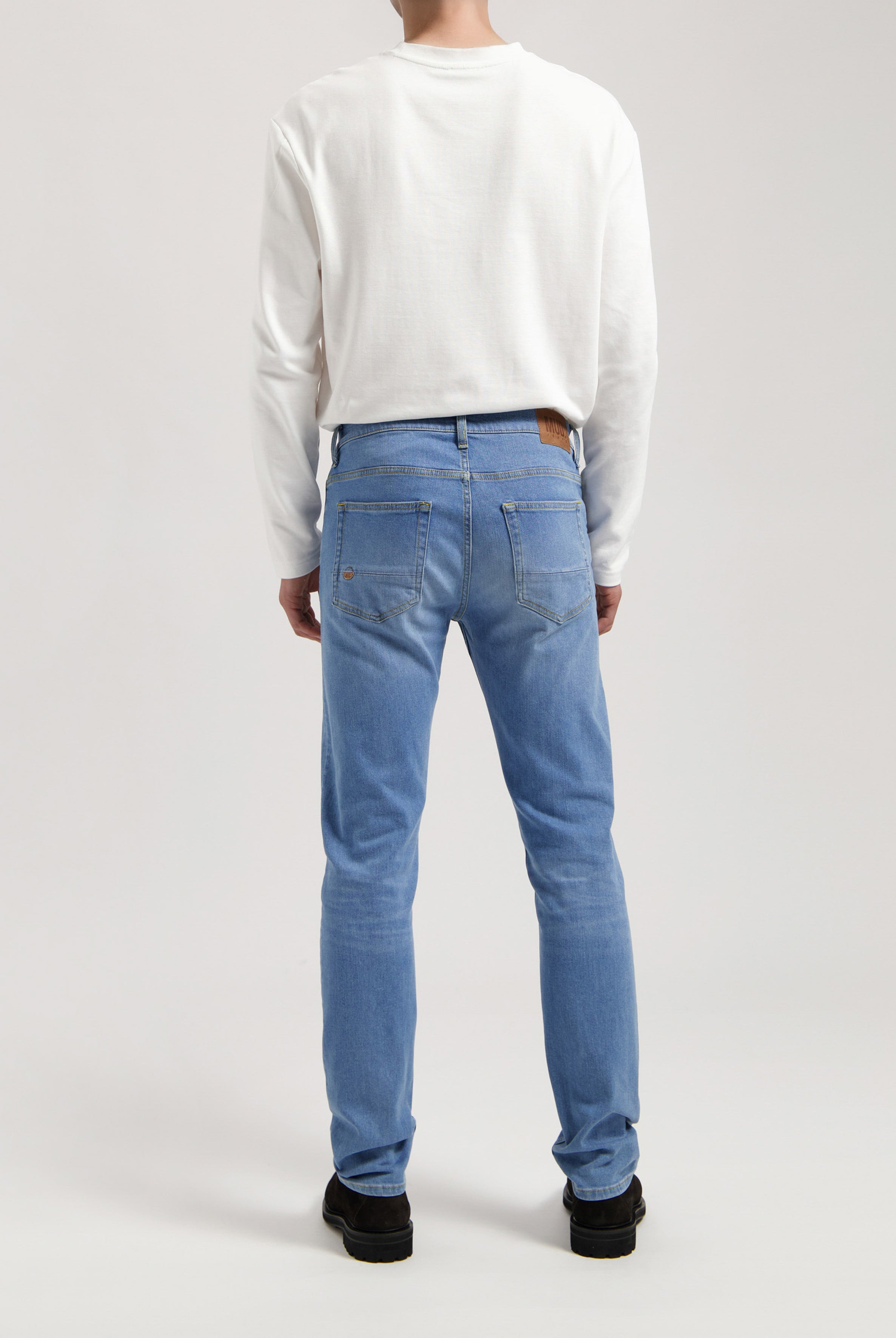 Eco-friendly MUD Jeans made from sustainable denim, deep blue color, worn with a soft gray sweater for ethical fashion.