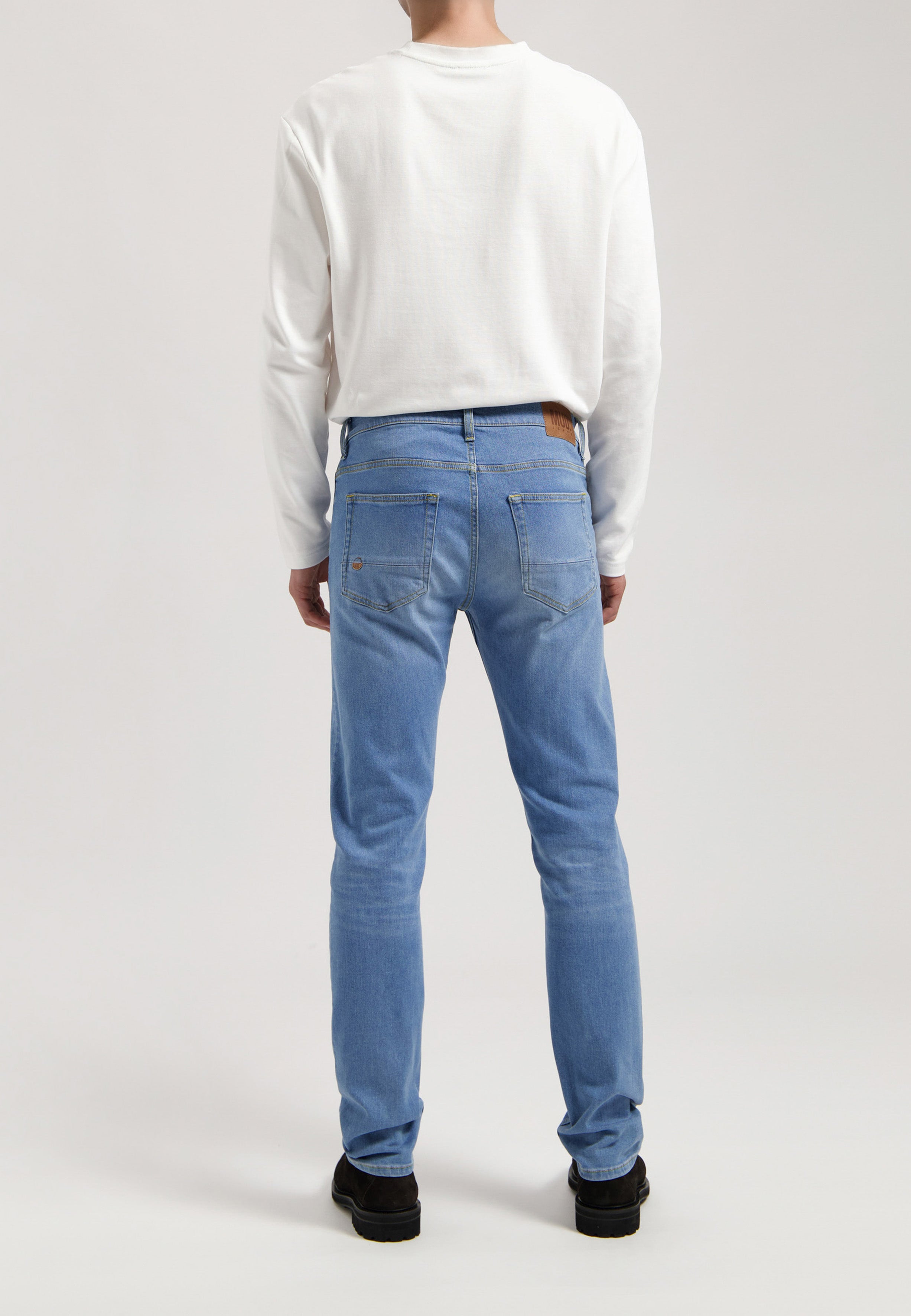 Eco-friendly MUD Jeans made from sustainable denim, deep blue color, worn with a soft gray sweater for ethical fashion.