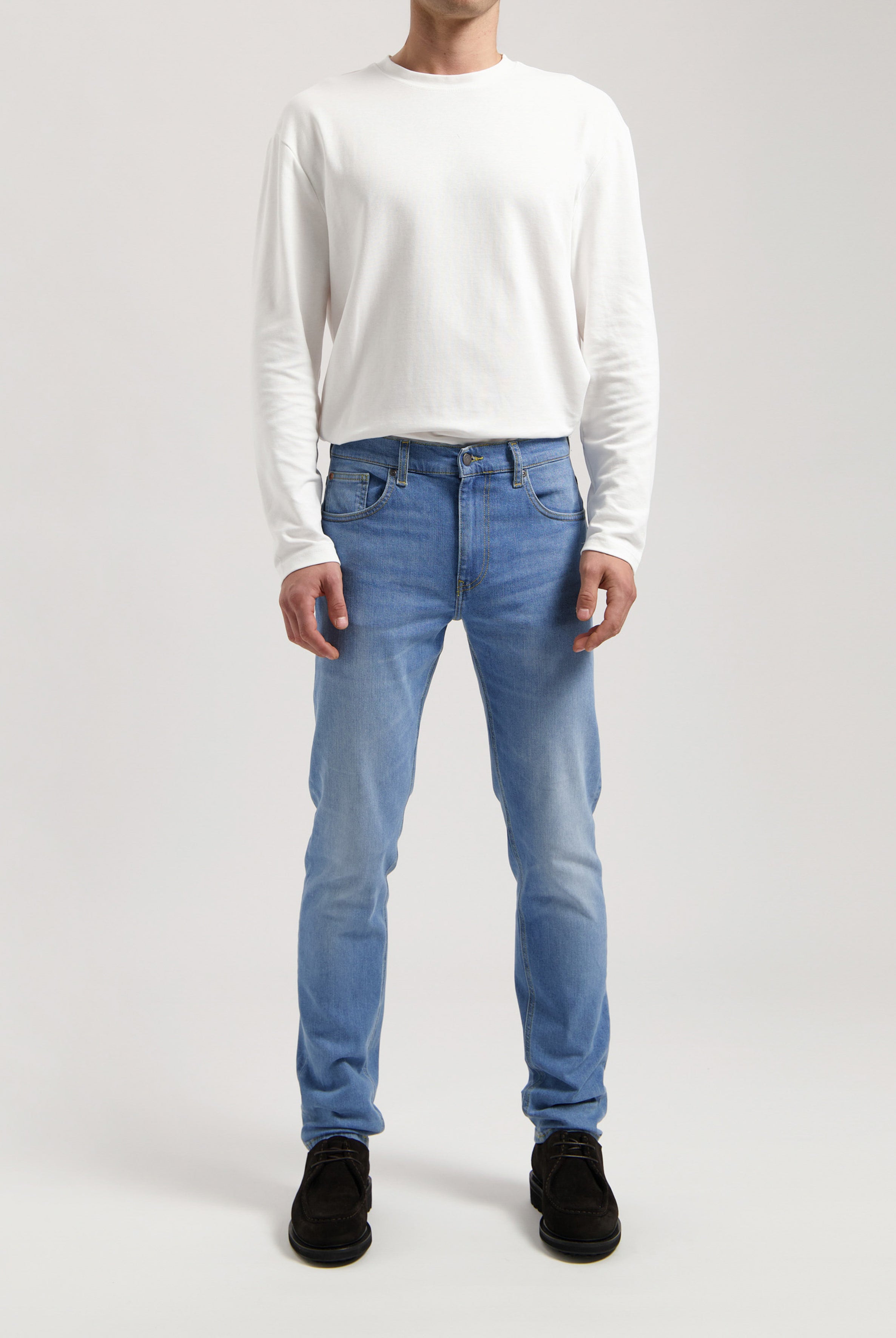 Sustainable MUD Jeans in blue denim, slim fit, made from ethical materials, paired with a gray sweater.