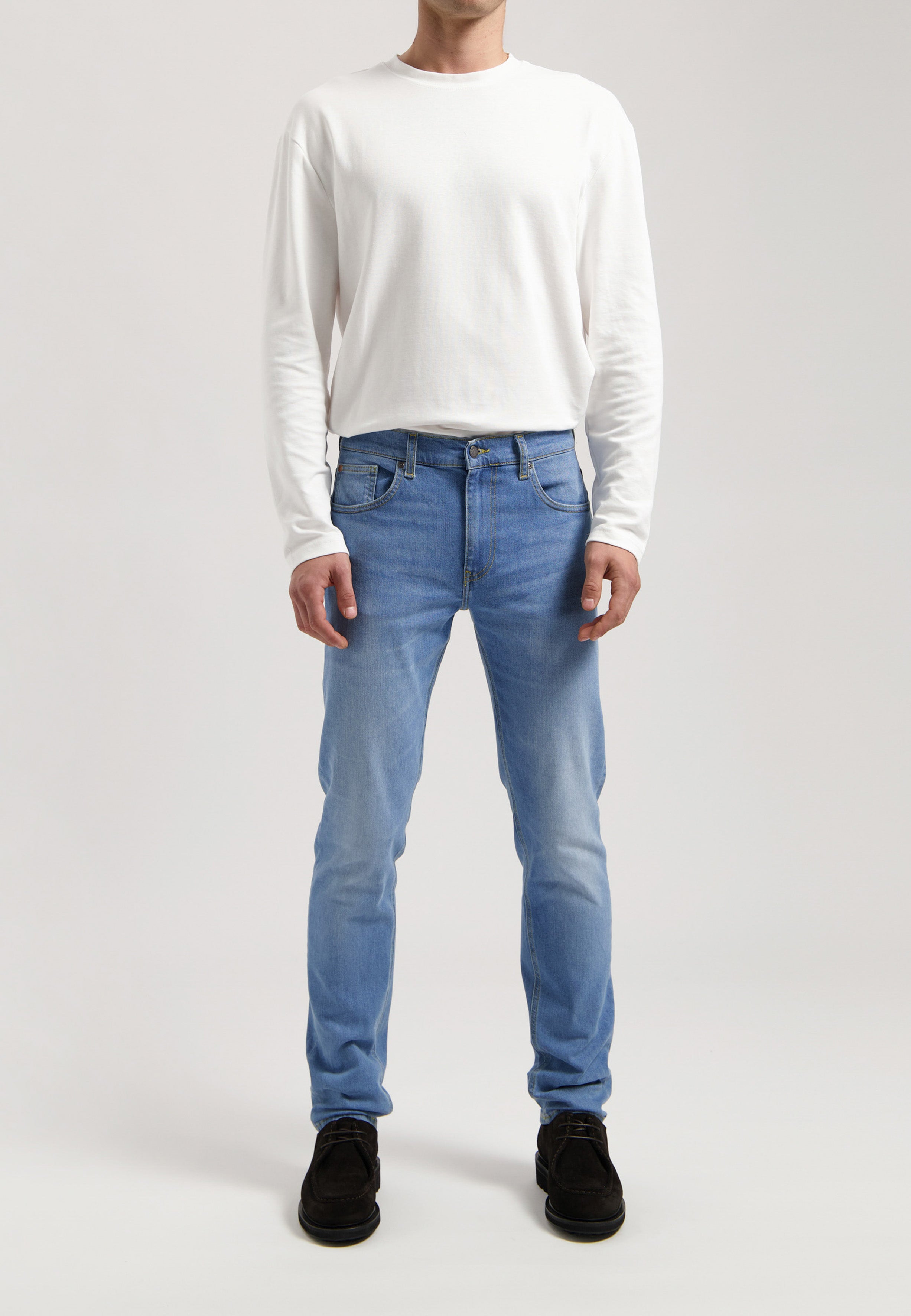 Sustainable MUD Jeans in blue denim, slim fit, made from ethical materials, paired with a gray sweater.