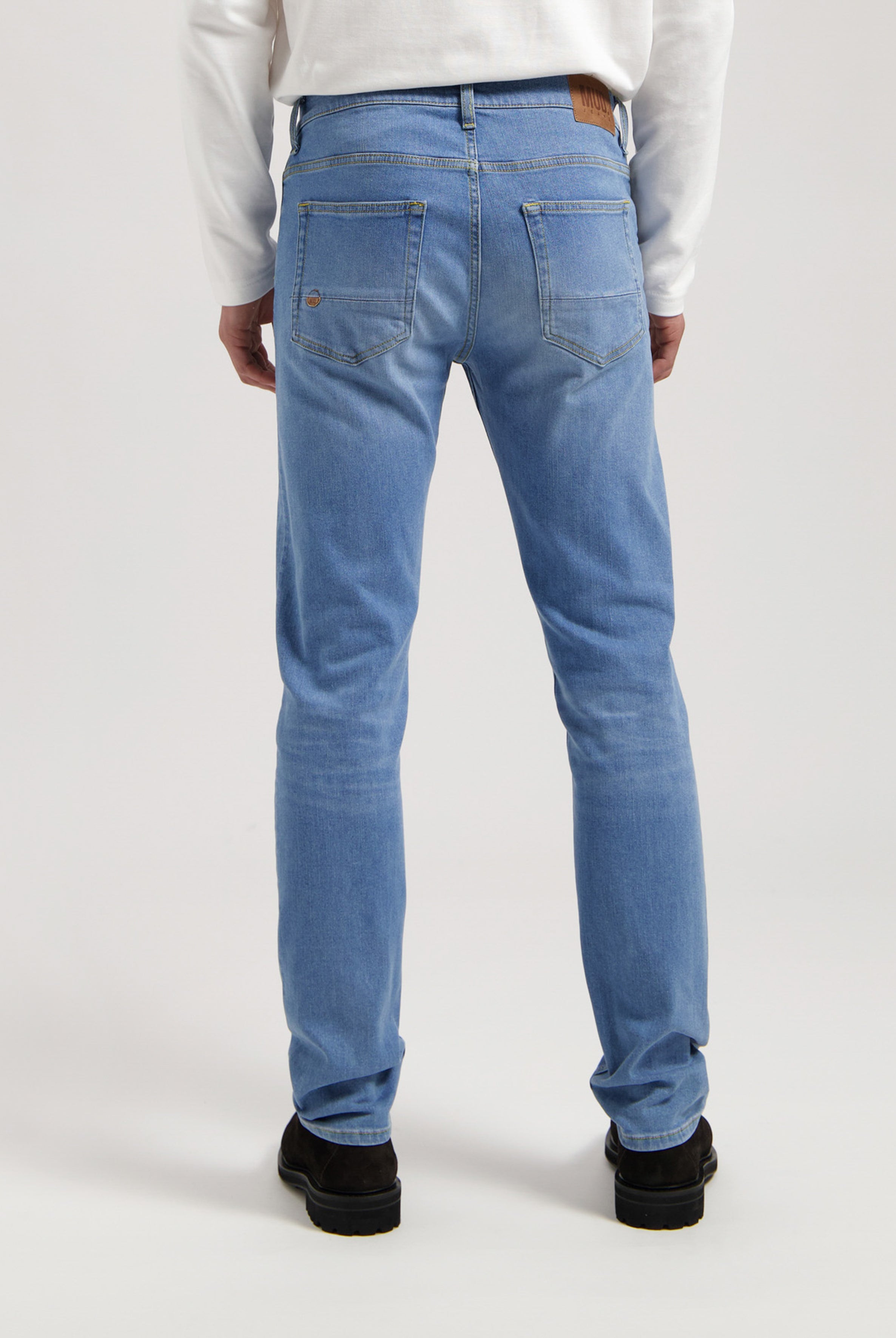 Sustainable Mud Jeans in light blue denim, crafted ethically, paired with a gray T-shirt and white sneakers.