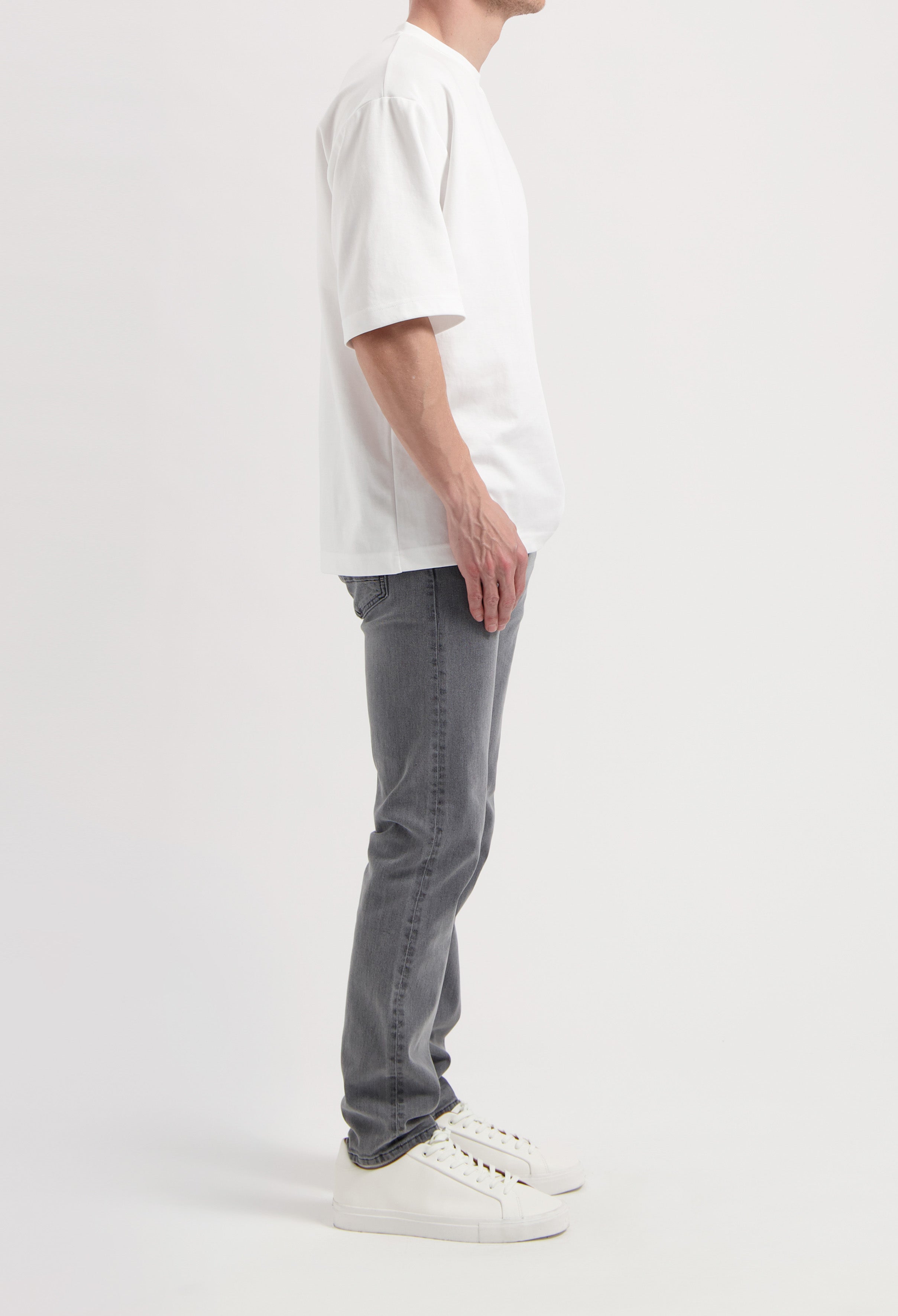 Sustainable MUD Jeans in gray denim, featuring a slim fit, paired with a black turtleneck and white sneakers.