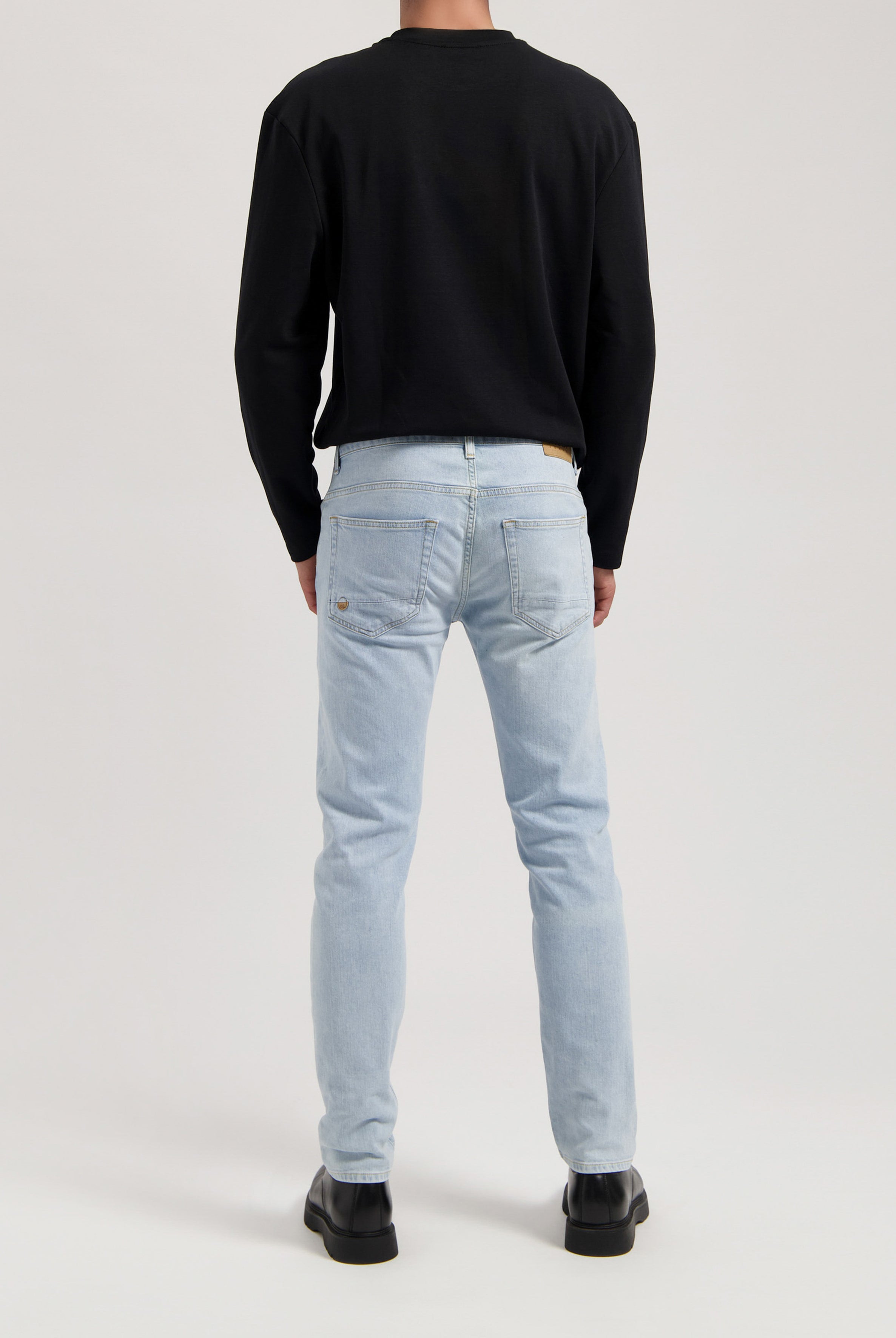 Sustainable MUD Jeans in light blue denim, crafted ethically from organic cotton, paired with a white long-sleeve shirt.