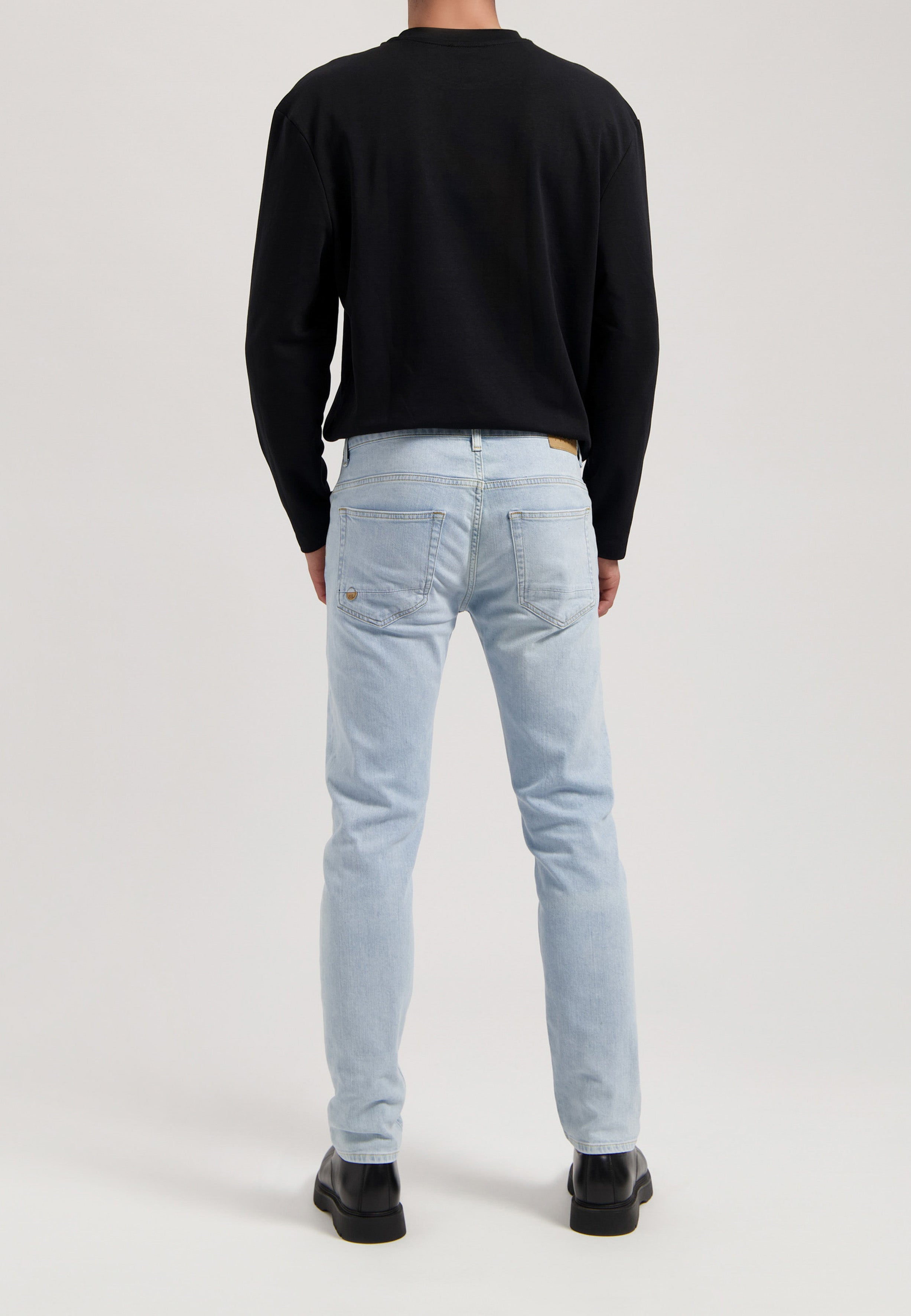 Sustainable MUD Jeans in light blue denim, crafted ethically from organic cotton, paired with a white long-sleeve shirt.