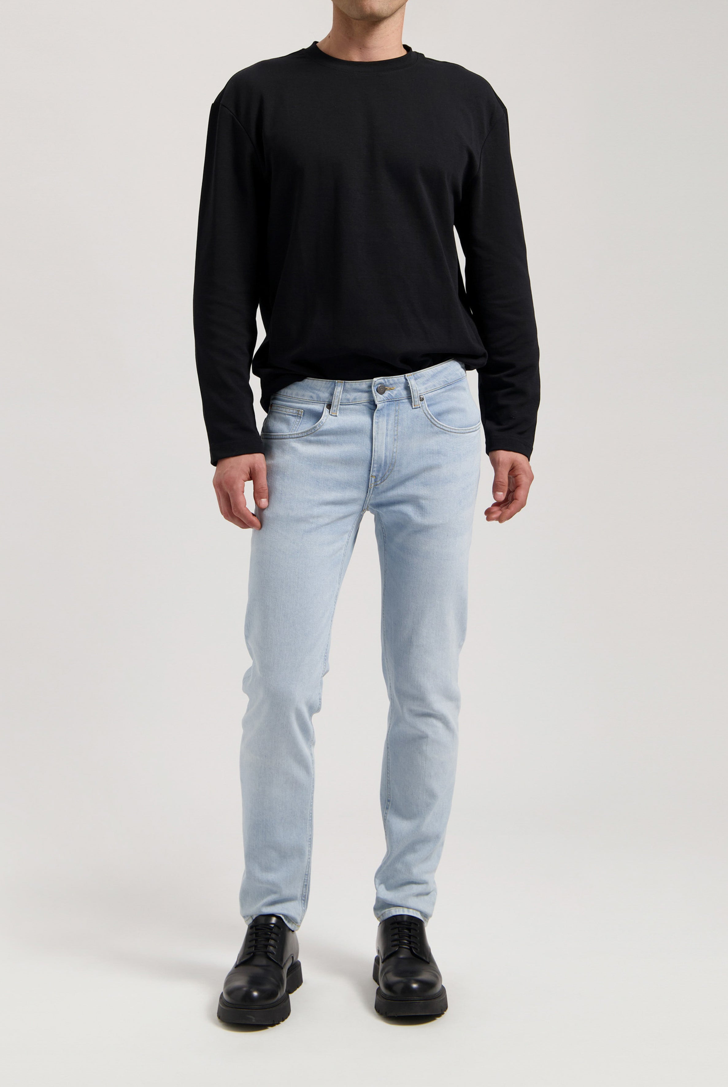 Sustainable MUD Jeans in light blue denim, crafted from organic cotton, shown in a side profile view with black shoes.