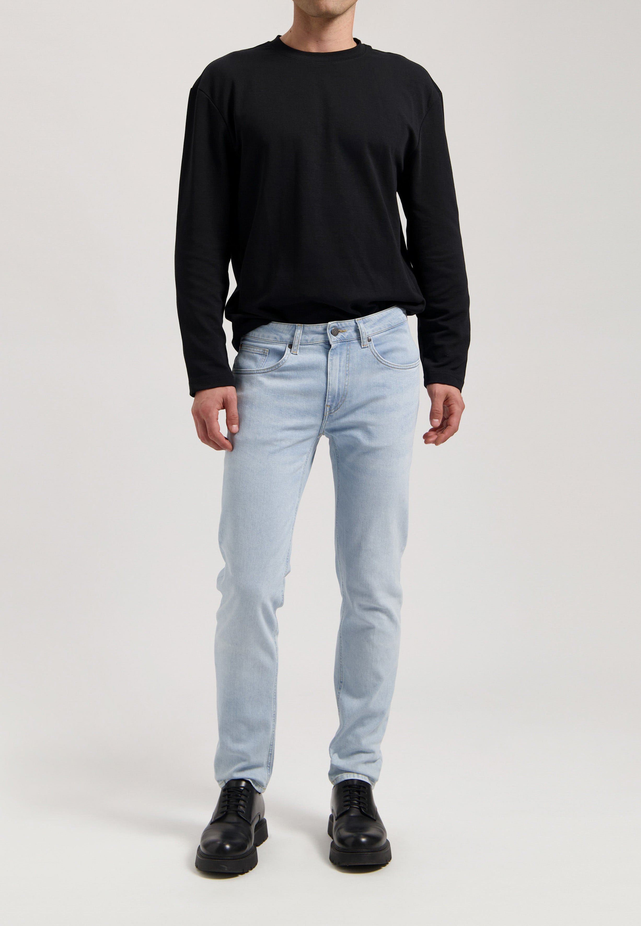Sustainable MUD Jeans in light blue denim, crafted from organic cotton, shown in a side profile view with black shoes.