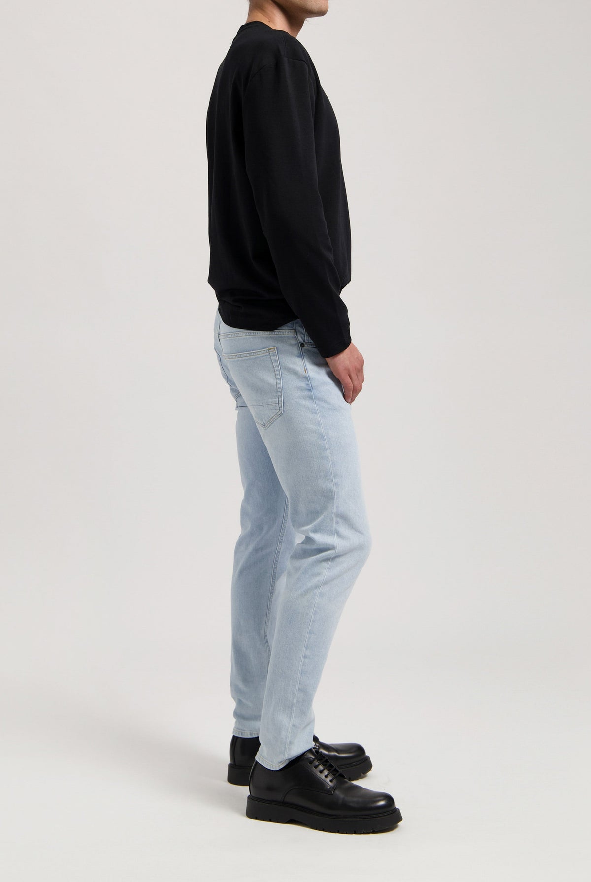 Sustainable MUD Jeans, light blue denim crafted ethically, paired with a white long-sleeve shirt, focusing on rear details.