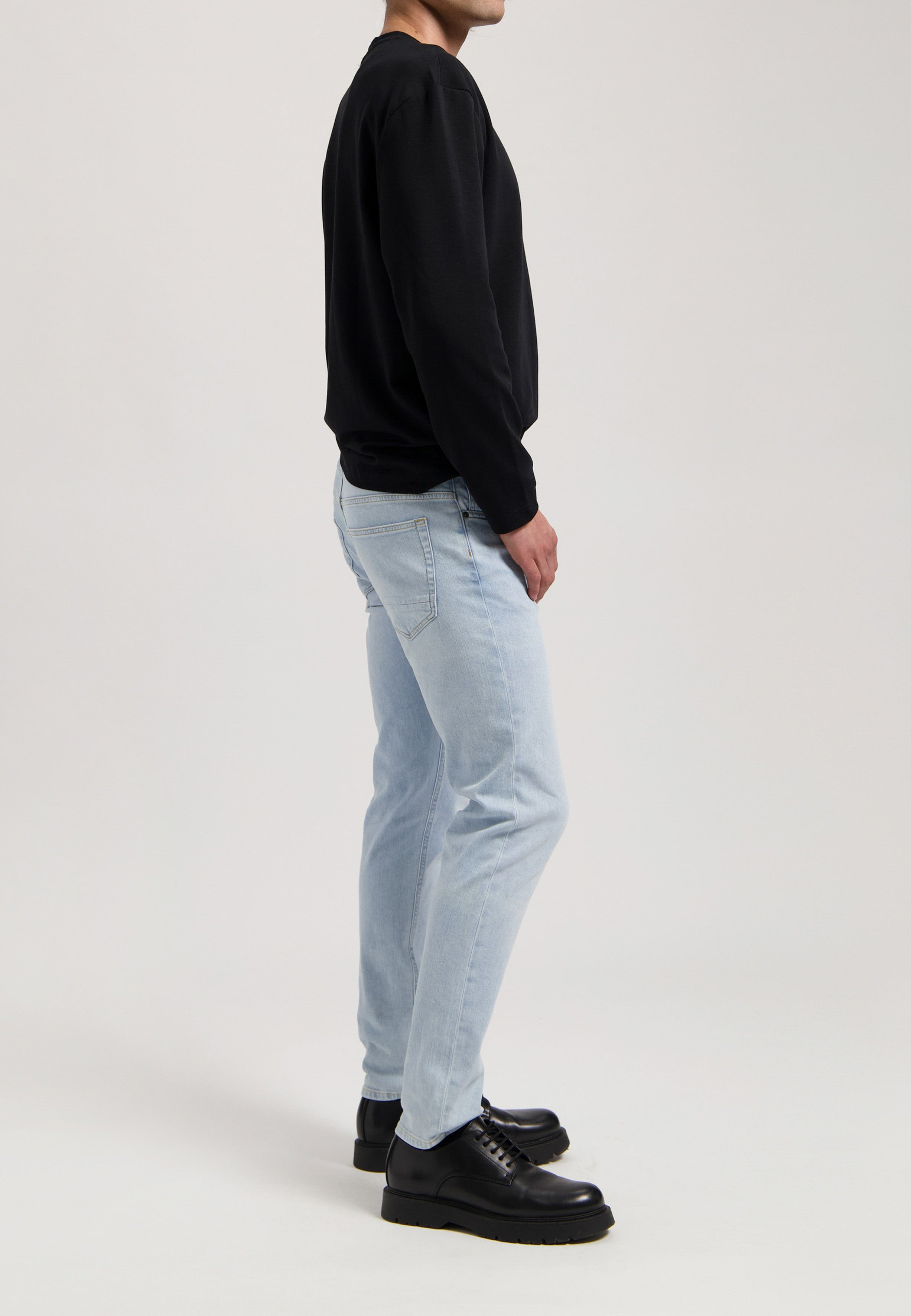Sustainable MUD Jeans, light blue denim crafted ethically, paired with a white long-sleeve shirt, focusing on rear details.