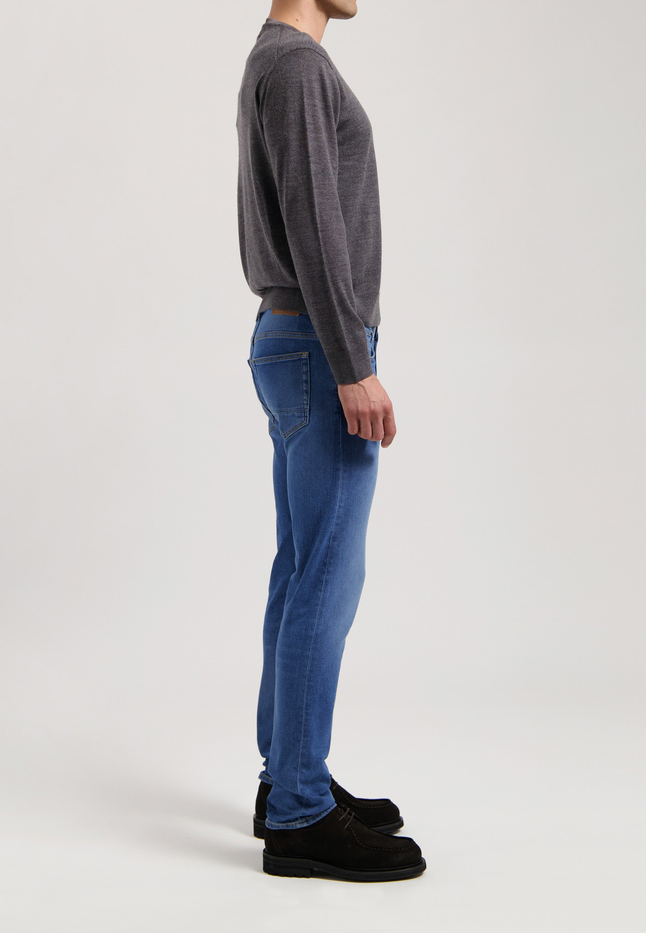 Sustainable MUD Jeans crafted from organic cotton, featuring classic blue denim, paired with a gray t-shirt and white sneakers.