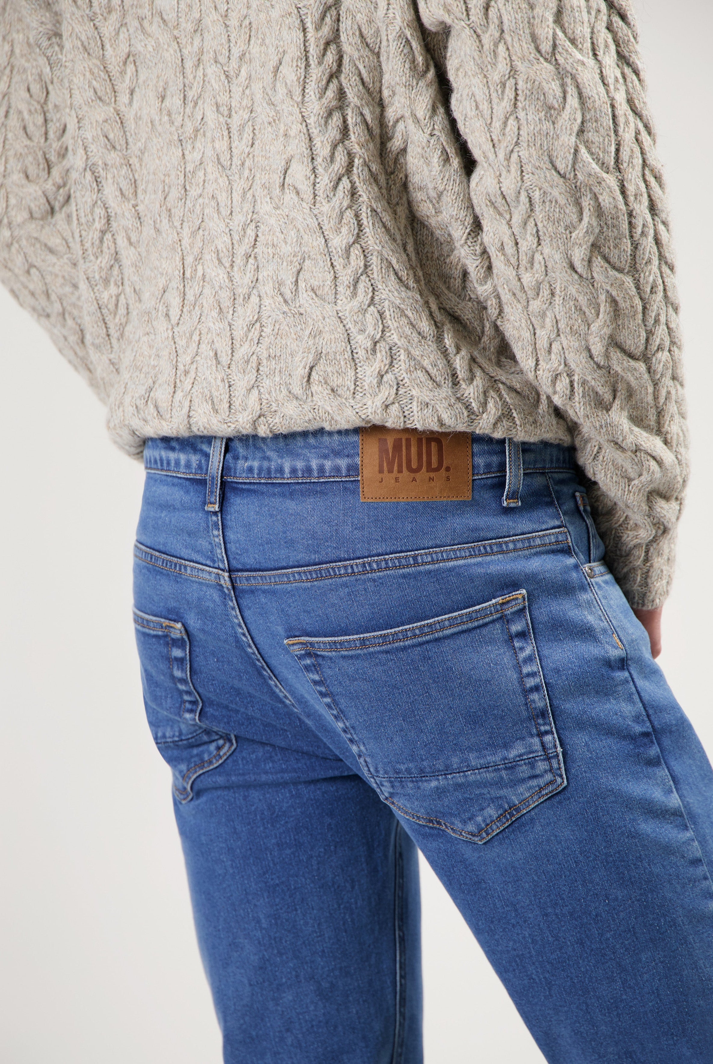 Sustainable MUD Jeans in blue denim, featuring classic fit and eco-friendly design, paired with a beige cable knit sweater.