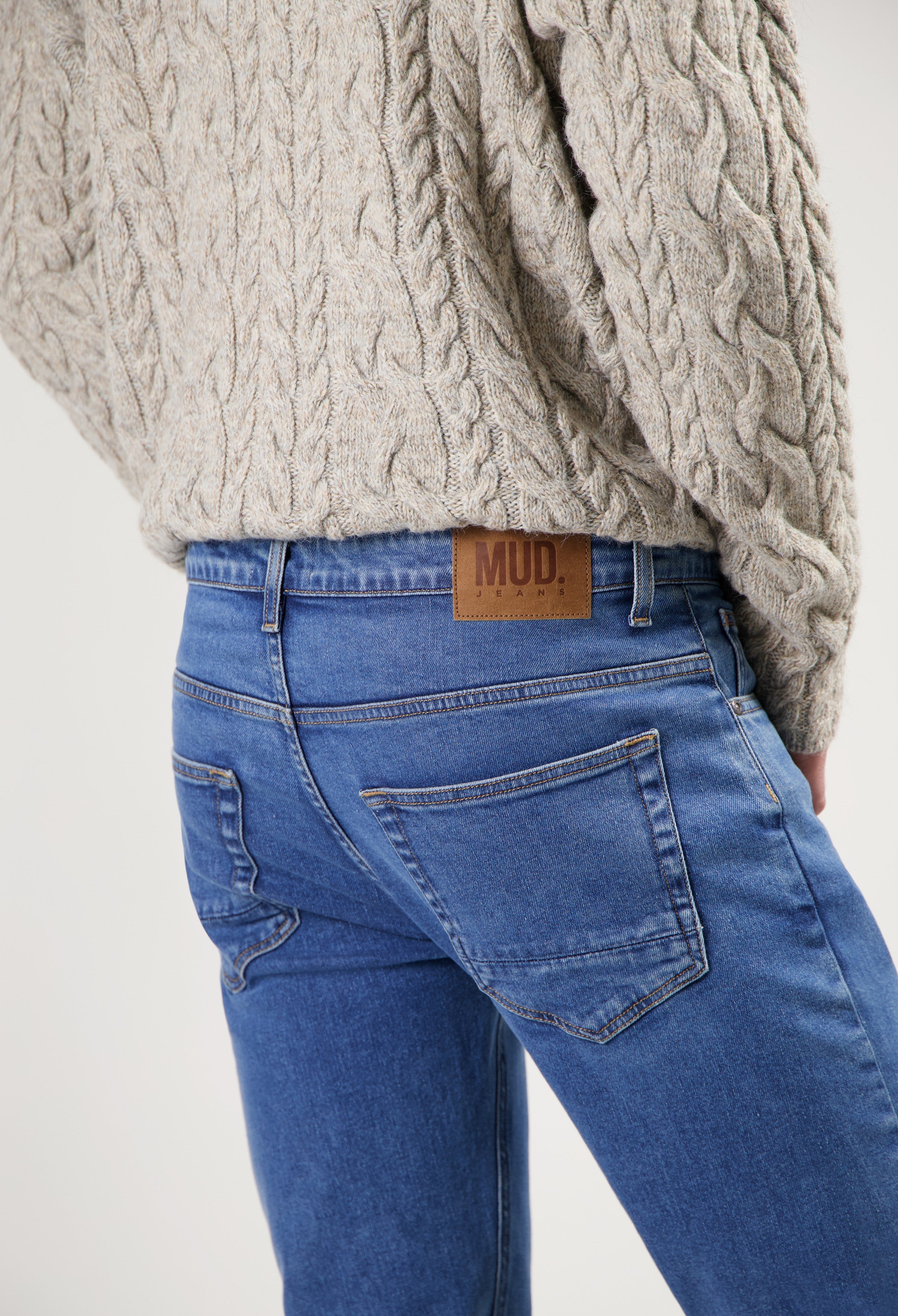 Sustainable MUD Jeans in blue denim, featuring classic fit and eco-friendly design, paired with a beige cable knit sweater.