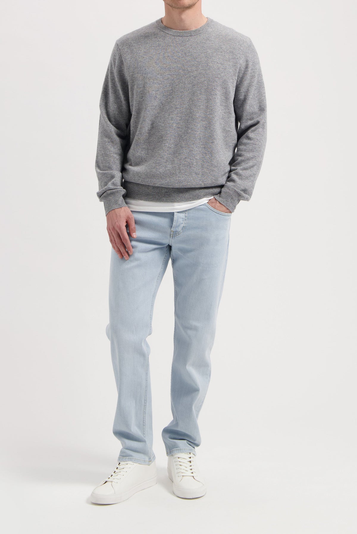 Sustainable MUD Jeans in gray denim, featuring an ethical, classic fit, paired with a black sweater and sneakers.