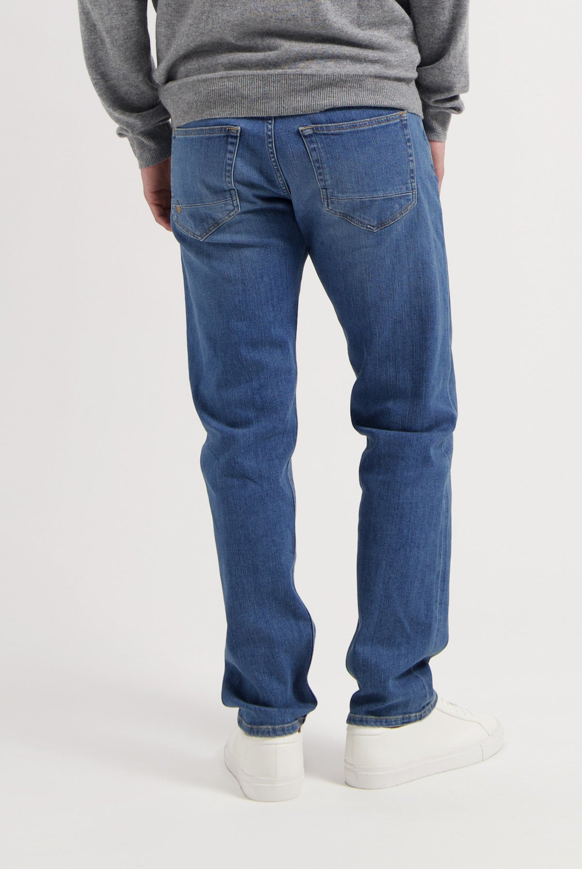 Sustainable MUD Jeans featuring dark blue denim, styled with a gray sweater and white sneakers for an ethical look.