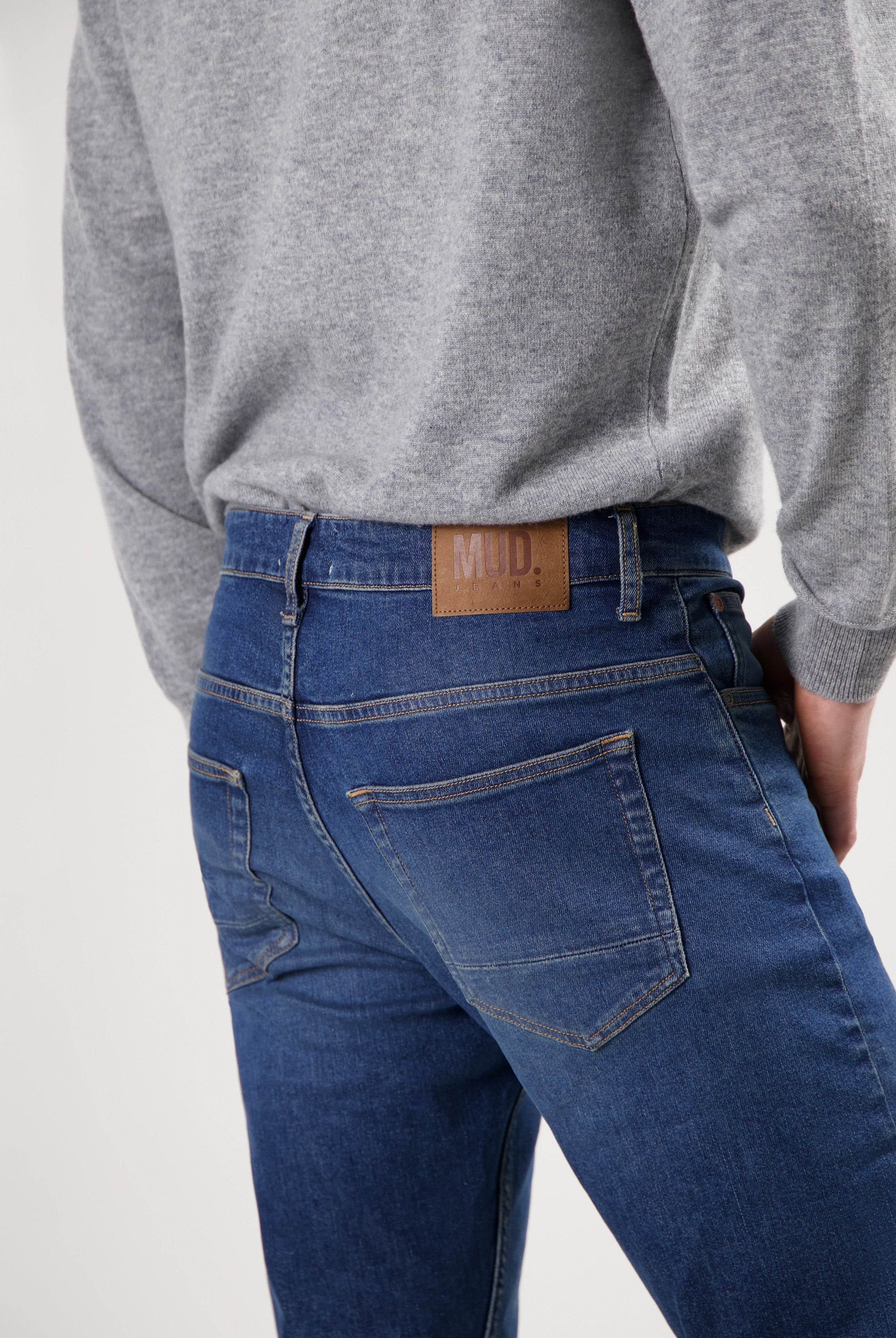 Sustainable MUD Jeans made from organic cotton, featuring deep blue denim in a modern fit, paired with a gray sweater.