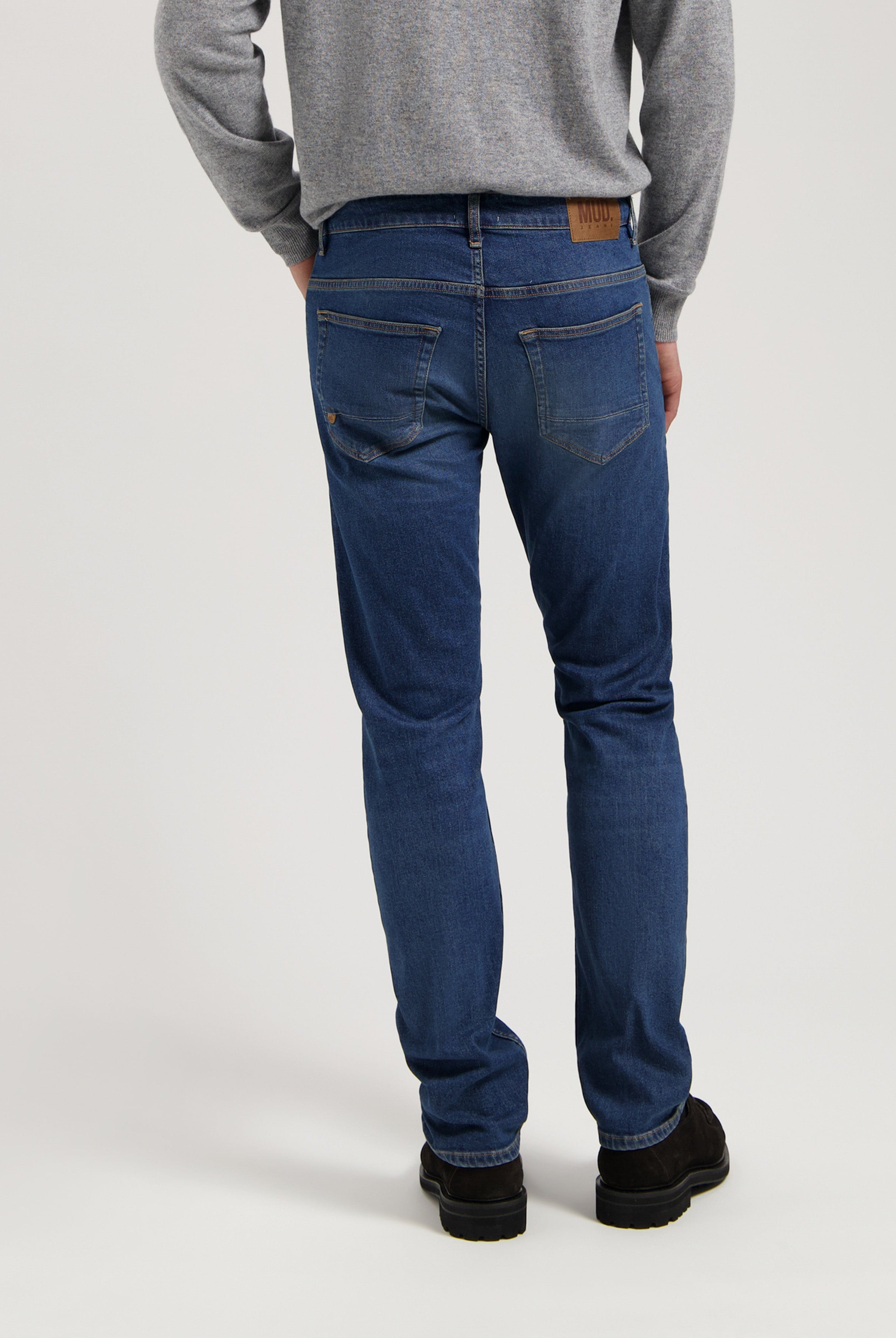 Sustainable MUD Jeans in dark blue denim, crafted from organic cotton, showcasing a relaxed fit, paired with a gray sweater.
