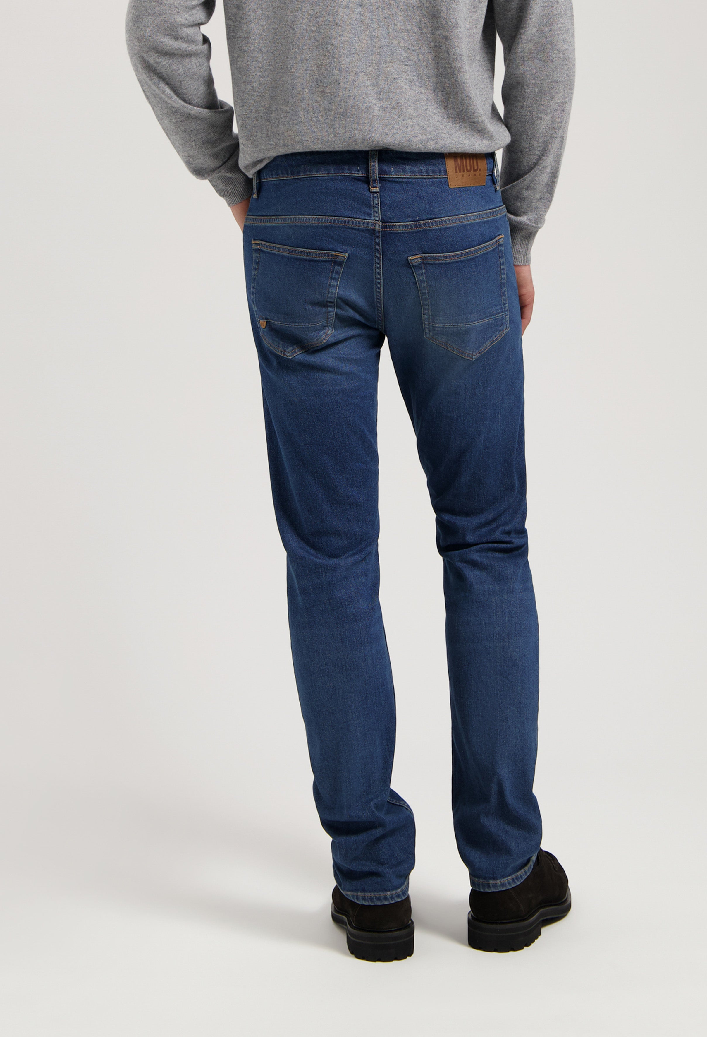 Sustainable MUD Jeans in dark blue denim, crafted from organic cotton, showcasing a relaxed fit, paired with a gray sweater.