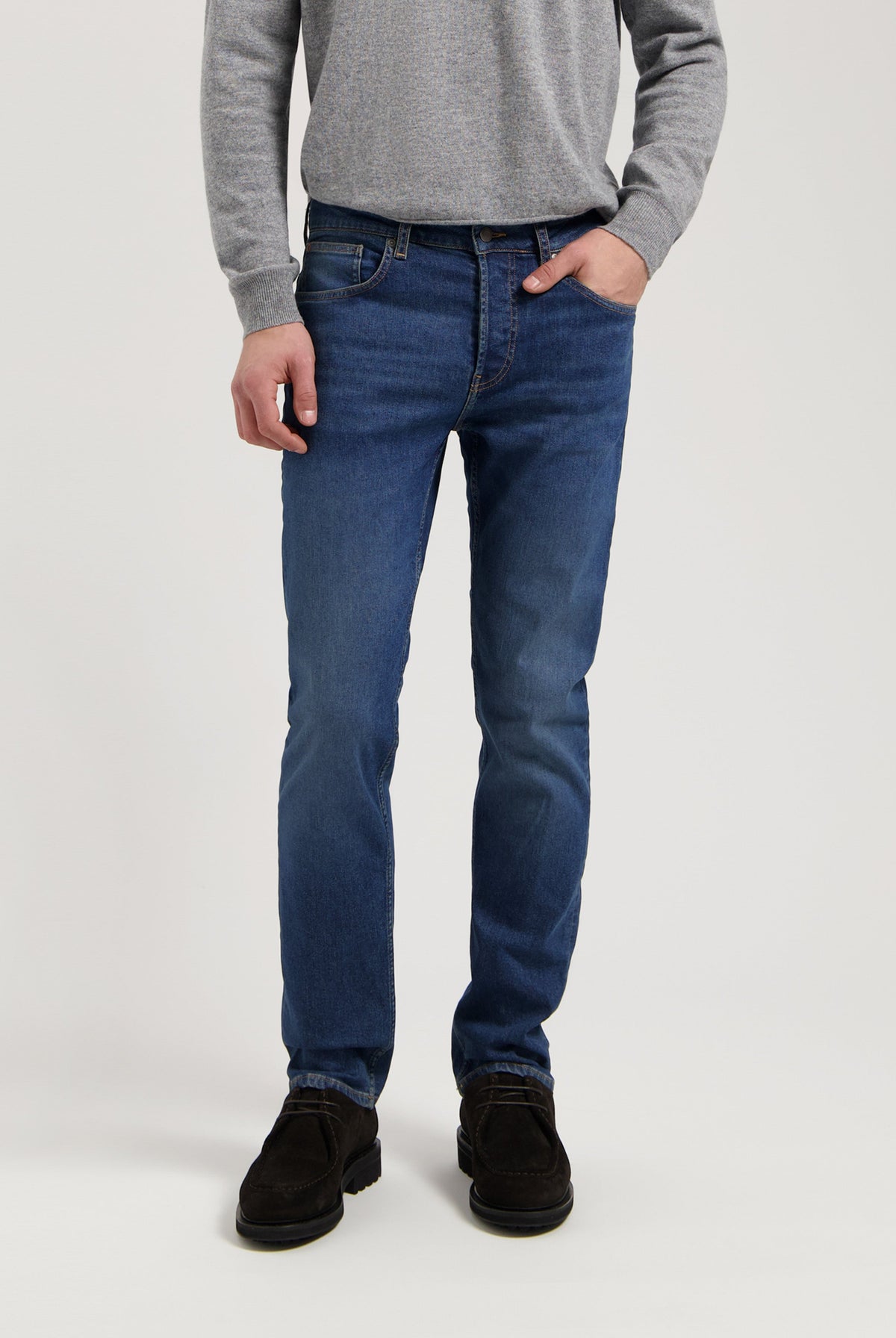 Sustainable MUD Jeans in classic fit, crafted from ethical materials in dark blue denim, worn with gray sweater.