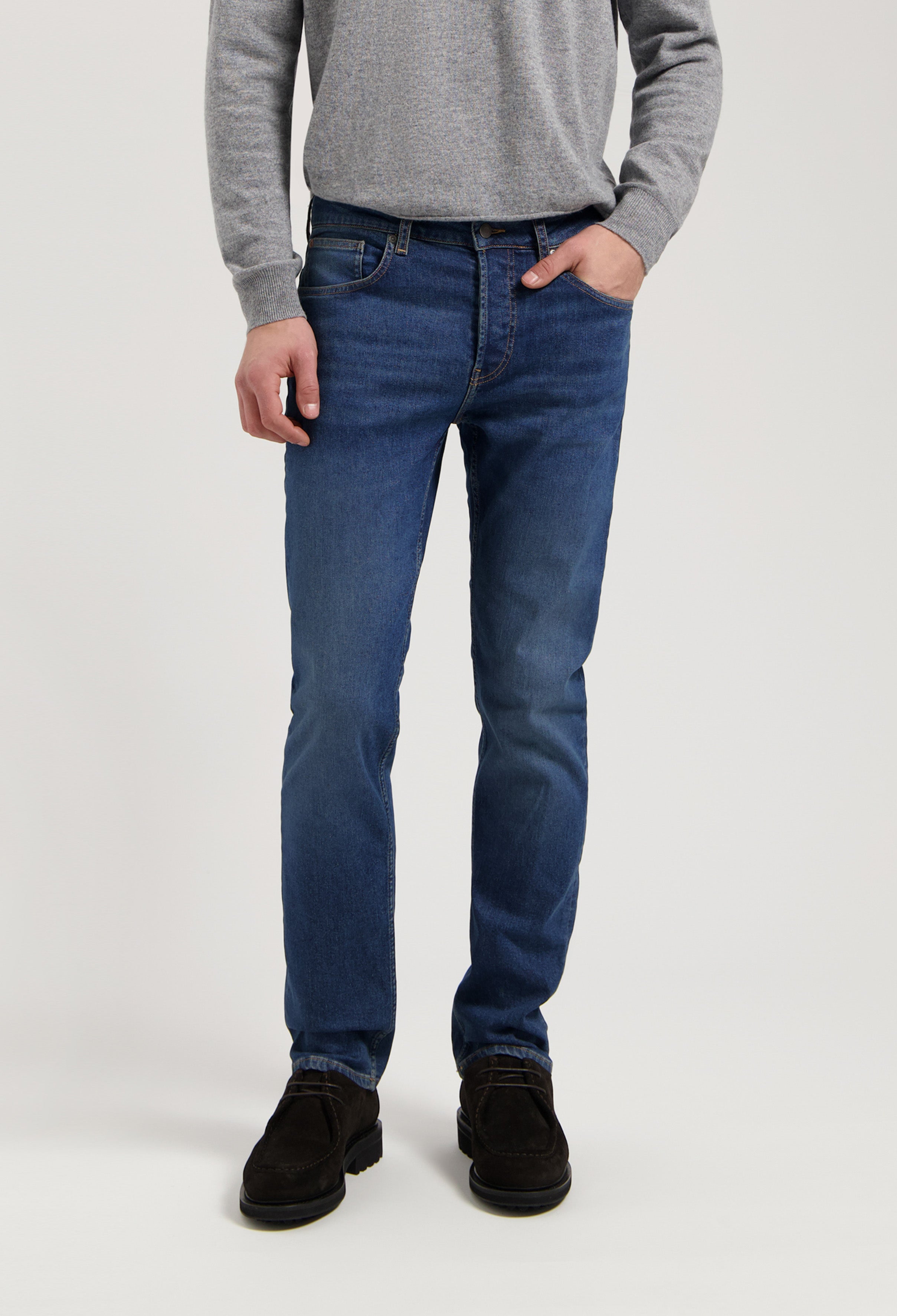 Sustainable MUD Jeans in classic fit, crafted from ethical materials in dark blue denim, worn with gray sweater.