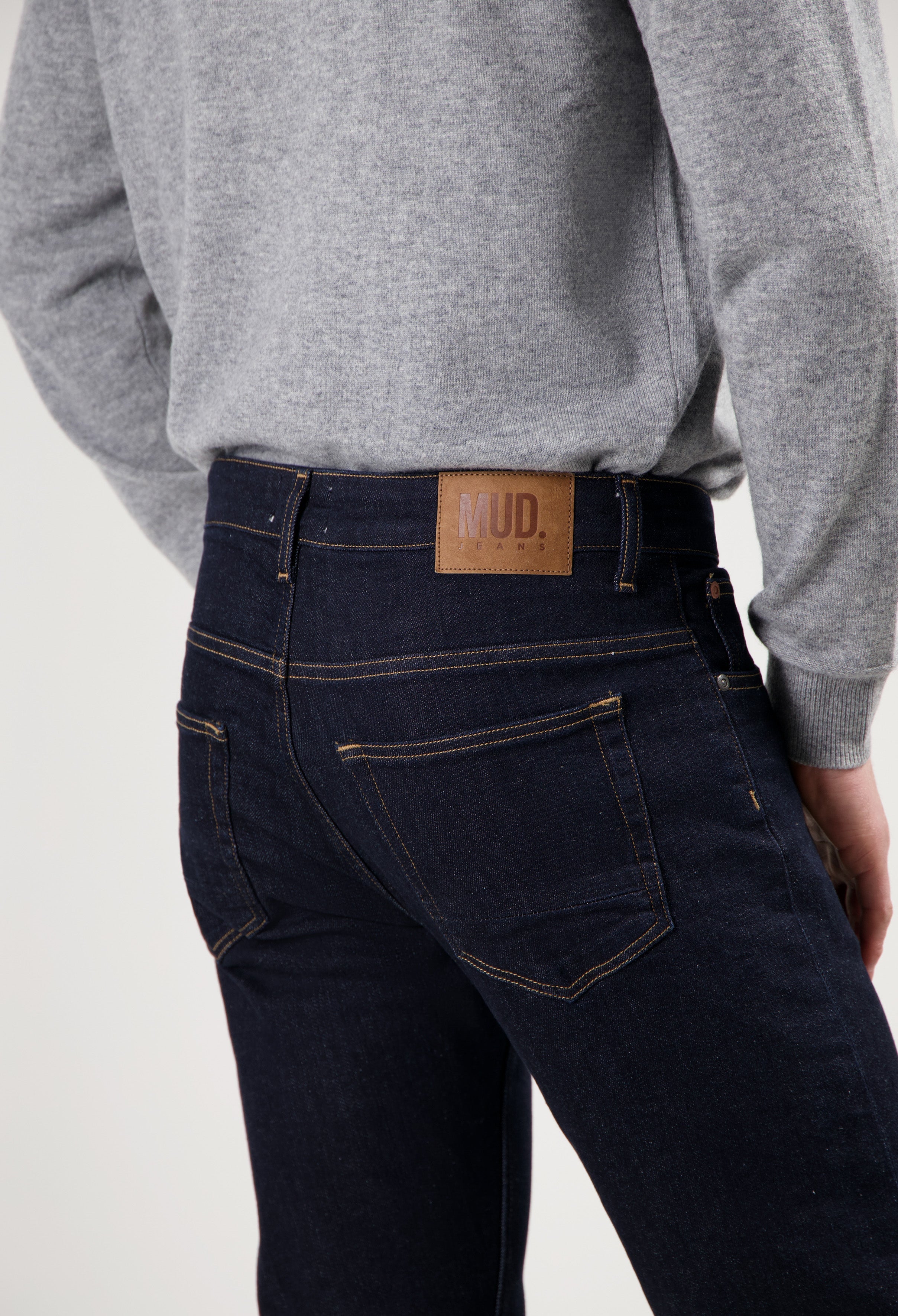 Sustainable MUD Jeans in dark blue denim, crafted from organic cotton, paired with a soft gray sweater for ethical style.
