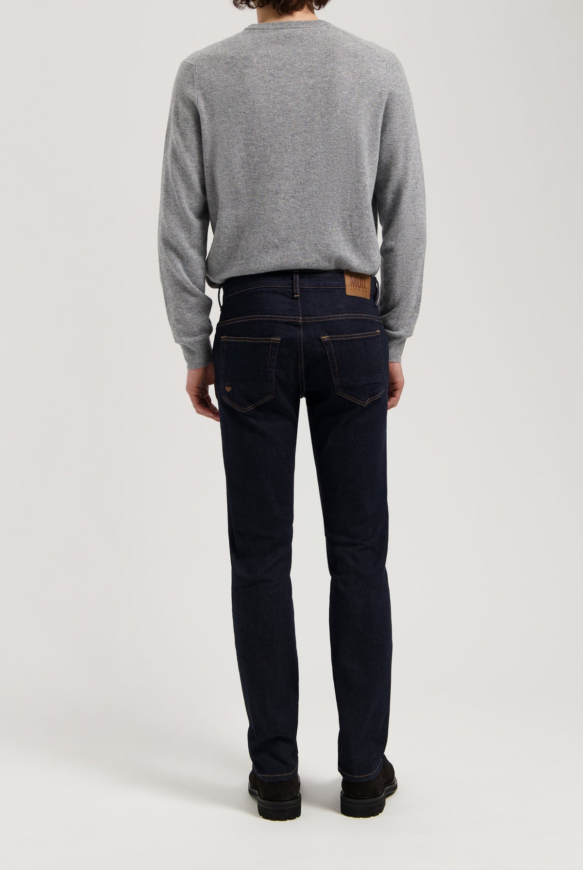Sustainable MUD Jeans in dark denim, crafted ethically, paired with a gray sweater for a classic, eco-friendly style.
