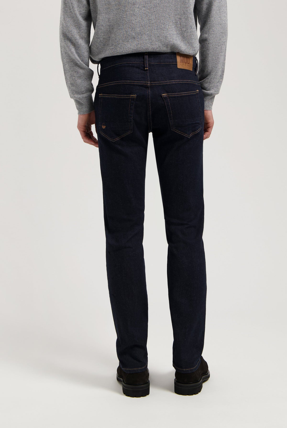 Sustainable MUD Jeans in dark denim, featuring ethical craftsmanship and classic stitch detail, paired with a gray sweater.