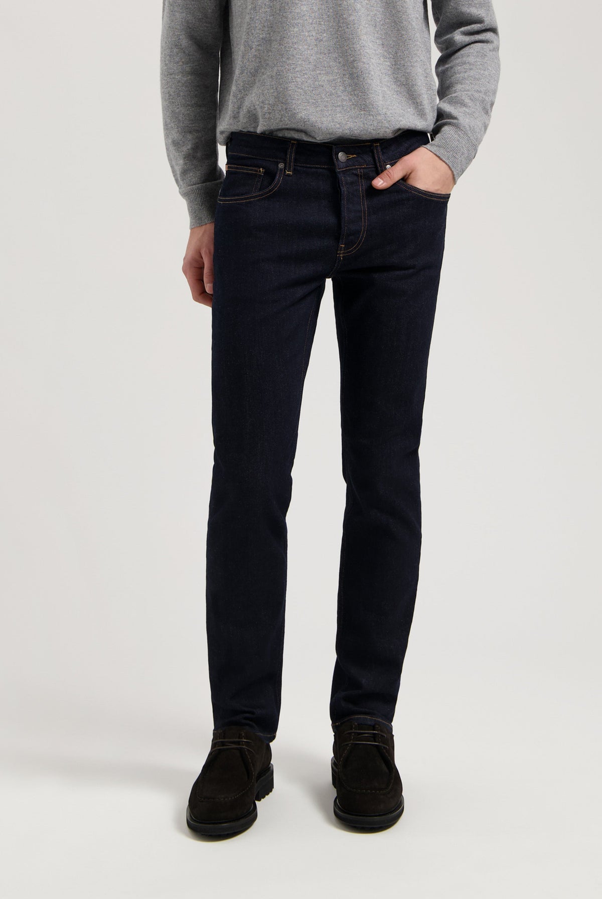 Sustainable MUD Jeans in dark blue organic cotton, featuring a slim fit design, paired with a cozy gray sweater.