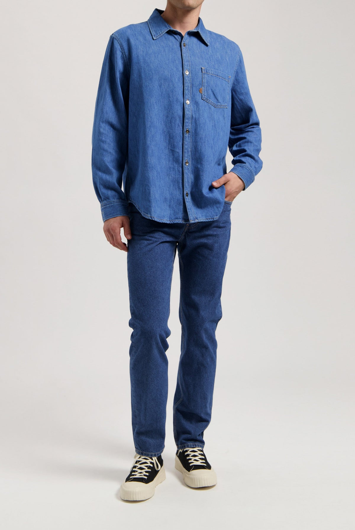 Sustainable MUD Jeans in deep indigo, made from organic cotton, paired with a simple white long-sleeved shirt.